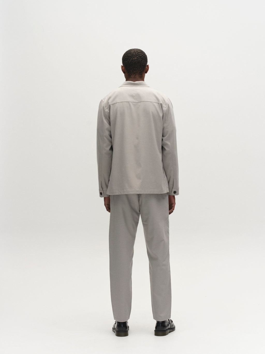 A person faces away from the camera, wearing the Gabba GABtogger Base Deme LS Overshirt in Mineral Gray against a plain white background for a minimal, test shot-like look.