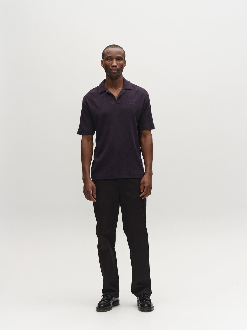 A man stands against a plain white background, wearing the Gabba GABlio Sku Towel T-Shirt in Night Sky. He pairs it with dark pants and black shoes, facing the camera with a neutral expression and his arms relaxed at his sides.