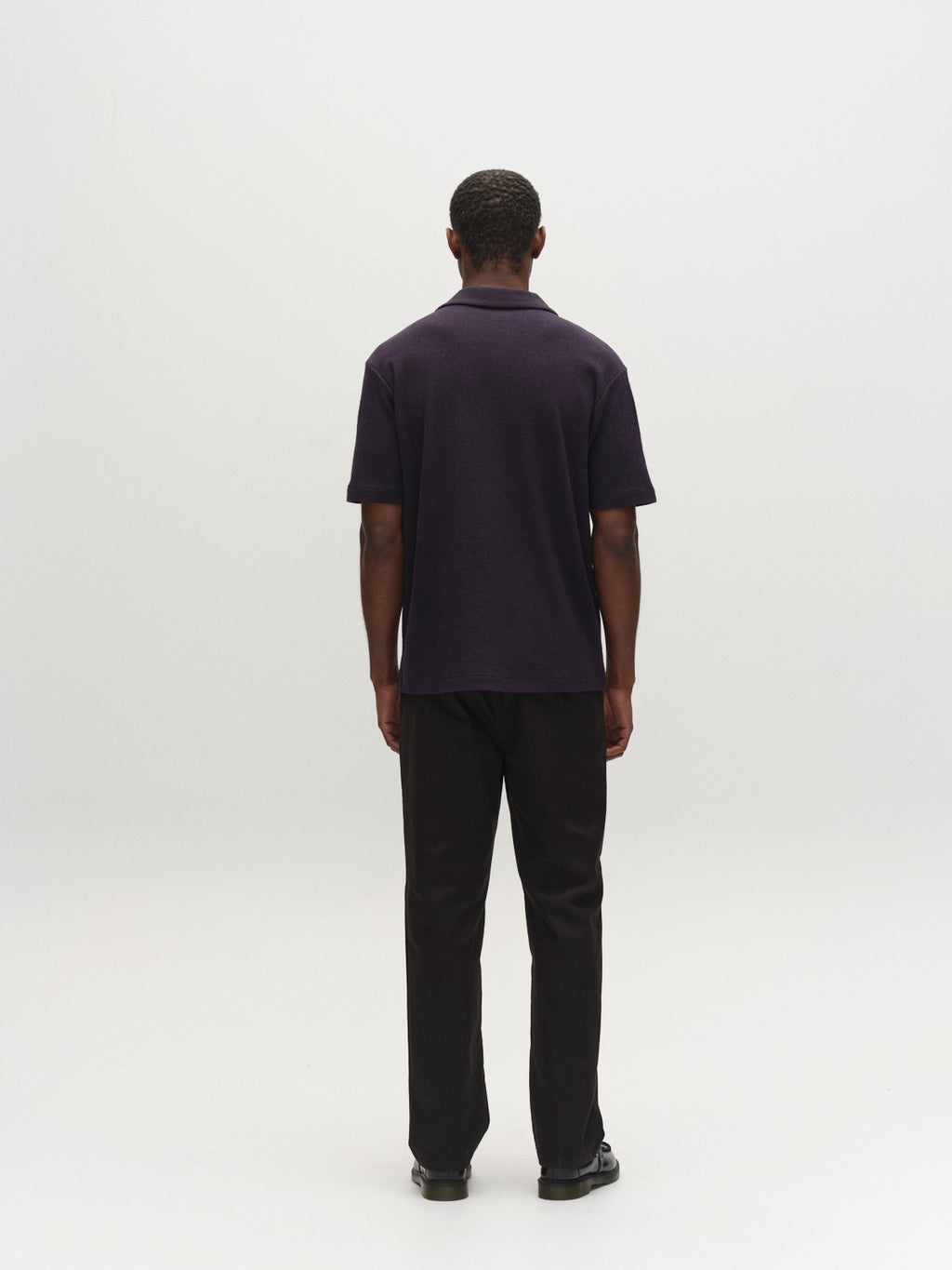 A man faces away from the camera, wearing the Gabba GABlio Sku Towel T-Shirt in Night Sky, paired with black pants and shoes, against a plain light background.