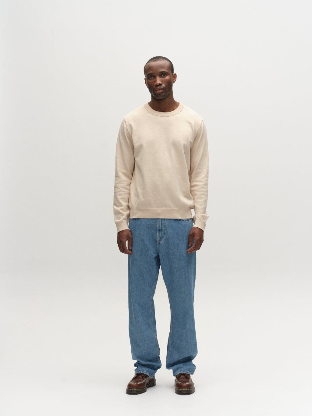 A man stands in a plain studio wearing the Gabba GABfumo Spy LS Knit in Sand, paired with blue jeans and brown shoes. He faces forward with arms relaxed at his sides against a white background.