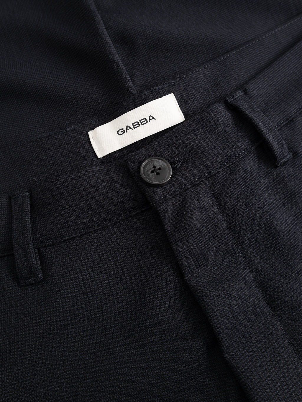 Close-up of the GABpaul Deme Pant in Dark Navy by Gabba, featuring a button closure and a white Gabba label sewn inside the waistband, crafted from micro-pattern woven fabric in a slim chino fit—perfect for everyday wear.
