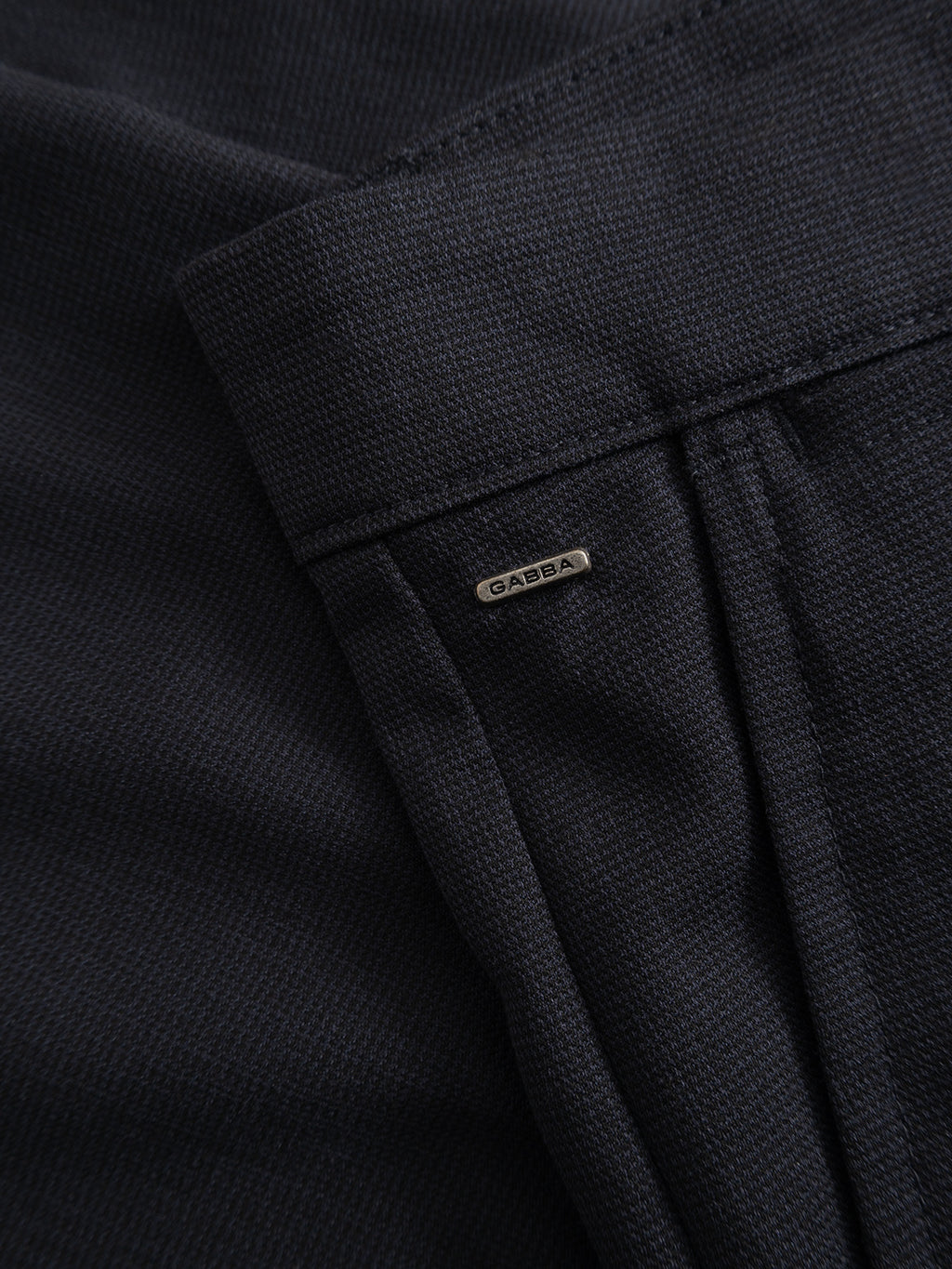 Close-up of the Gabba GABpaul Deme Pant in dark navy, featuring a dark micro-pattern woven fabric and a slim chino fit, accented by a small metallic Gabba tag sewn near the seam—perfect for everyday wear.