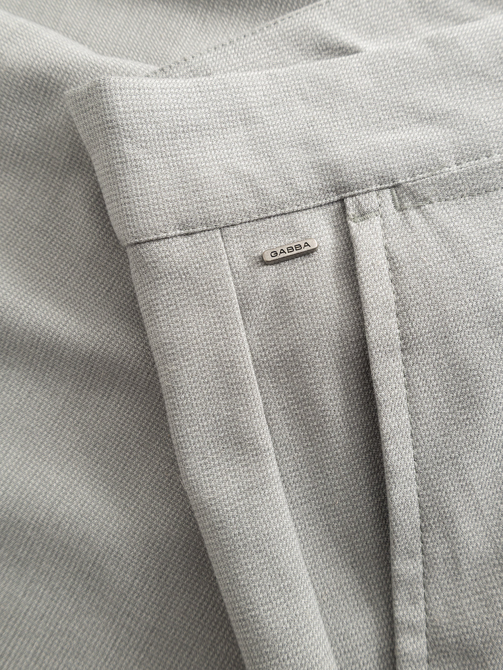 Close-up of GABpaul Deme Pant by Gabba in Mineral Gray, slim-fit with micro-pattern woven fabric, visible waistband, belt loop, and a metal tag labeled Gabba.