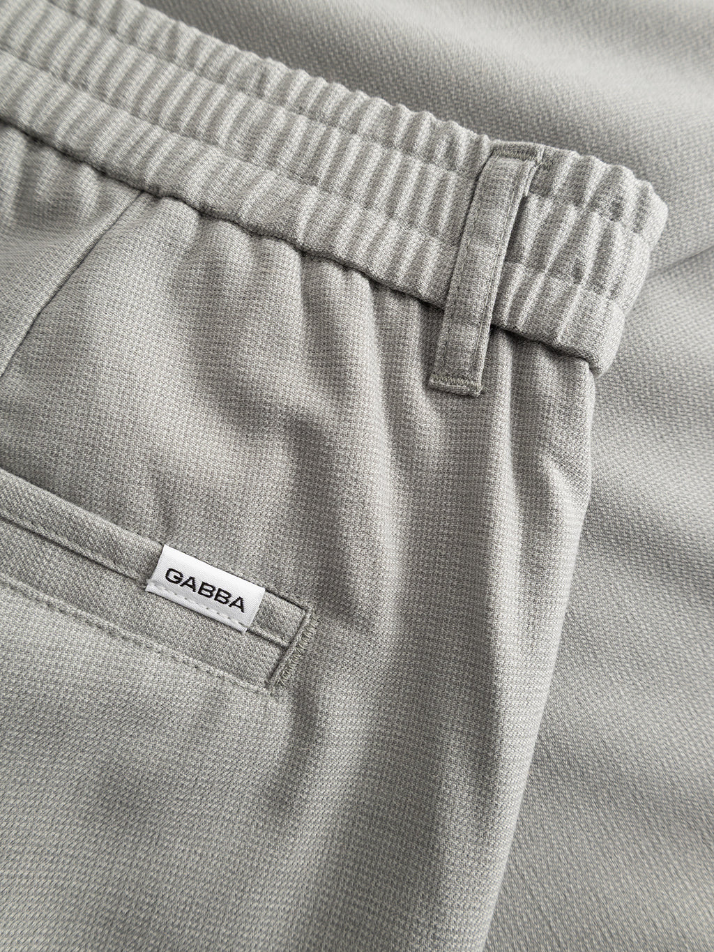 Close-up of Gabba’s GABmonza Tasca Deme Pant in Mineral Gray—soft, lightly textured linen with a relaxed straight fit, elastic waistband, belt loop, back pocket, and a white Gabba label.