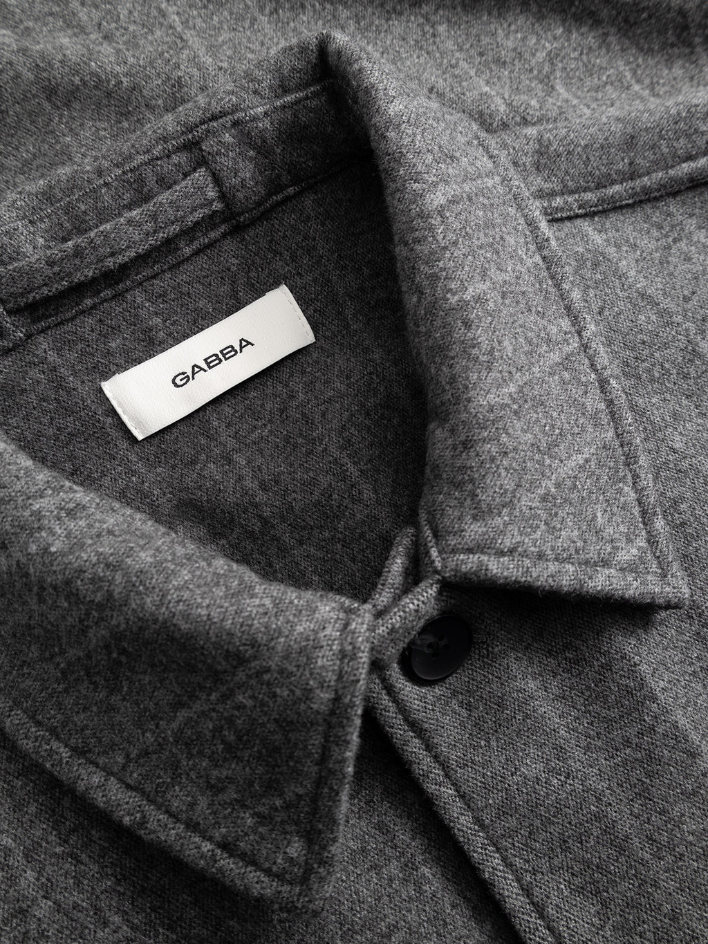 Close-up of the collar on the GABlibre AX Stripes LS Overshirt in Dark Grey by Gabba, featuring a black button and a white Gabba label sewn inside the neckline; showcases the viscose-blend fabric and boxy fit.