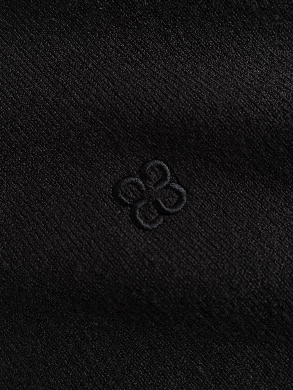 Close-up of the meteorite-colored fabric from the Gabba GABadriel Half Zip Lume LS Knit, showing a small, embroidered geometric flower-like pattern in matching black thread at the center.