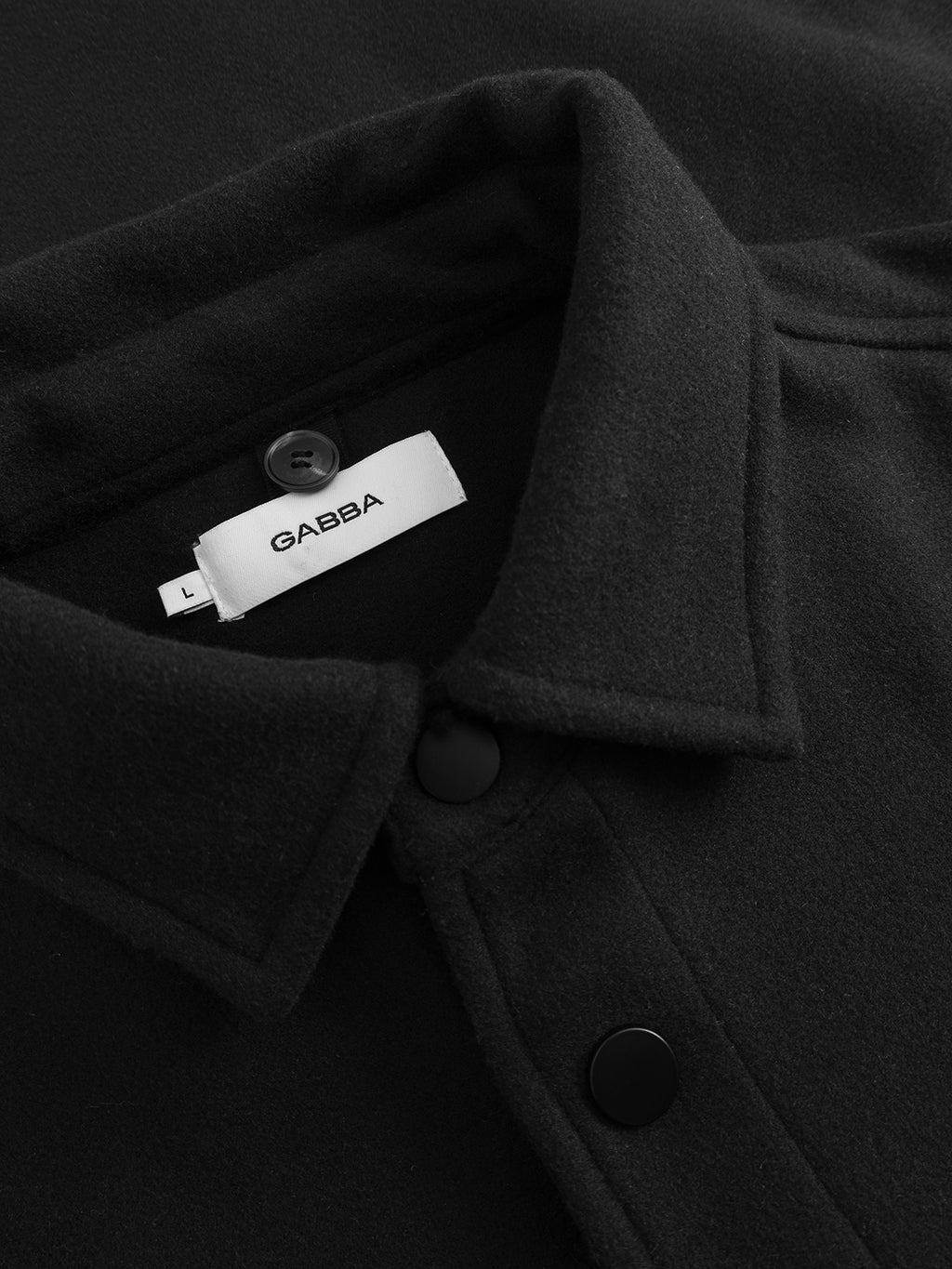Close-up of the GABtheo City Jacket in black by Gabba, featuring black buttons and a white Gabba label inside the collar, crafted from a wool-inspired fabric ideal for everyday layering.