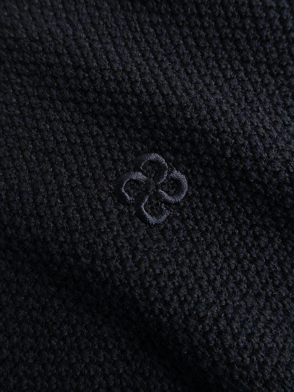Close-up of the GABlamix Coro Half LS Knit in Blue Black by Gabba, featuring dark, textured cotton-blend knit fabric with a subtle, small embroidered geometric pattern at the center.