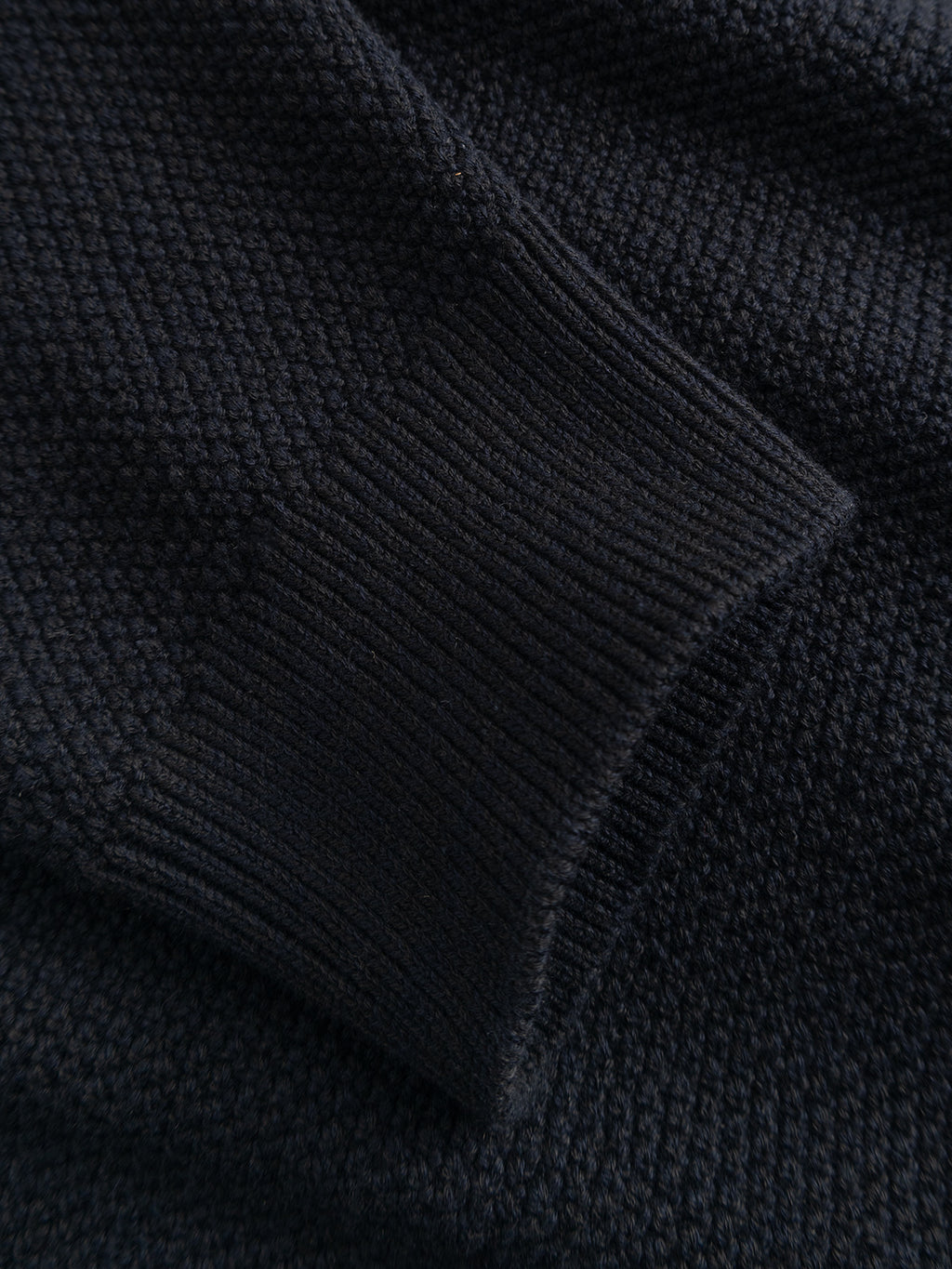 Close-up of the GABlamix Coro Half LS Knit in Blue Black by Gabba, featuring a textured dark cotton-blend knit fabric with a ribbed cuff detail on the sleeve. The material looks soft and substantial, characteristic of this regular fit sweater.