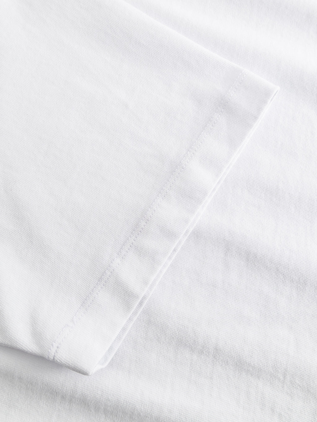 Close-up of the Gabba GABlegin Wix Boxy Hour SS T-shirt in white, highlighting the precisely stitched sleeve hem and soft cotton jersey fabric texture, laid flat against a white background.