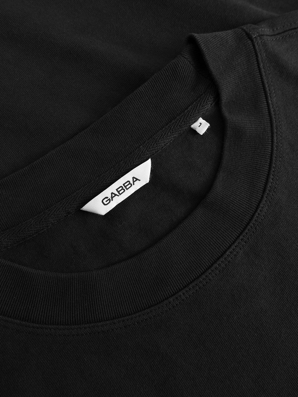 Close-up of the Gabba GABlegin Wix Boxy Hour SS T-shirt in black, featuring a white label inside the crew-neck collar with “Gabba” branding and a visible size tag marked ‘L’. Made from mid-weight cotton jersey, this tee is designed for comfort and durability in everyday wear.