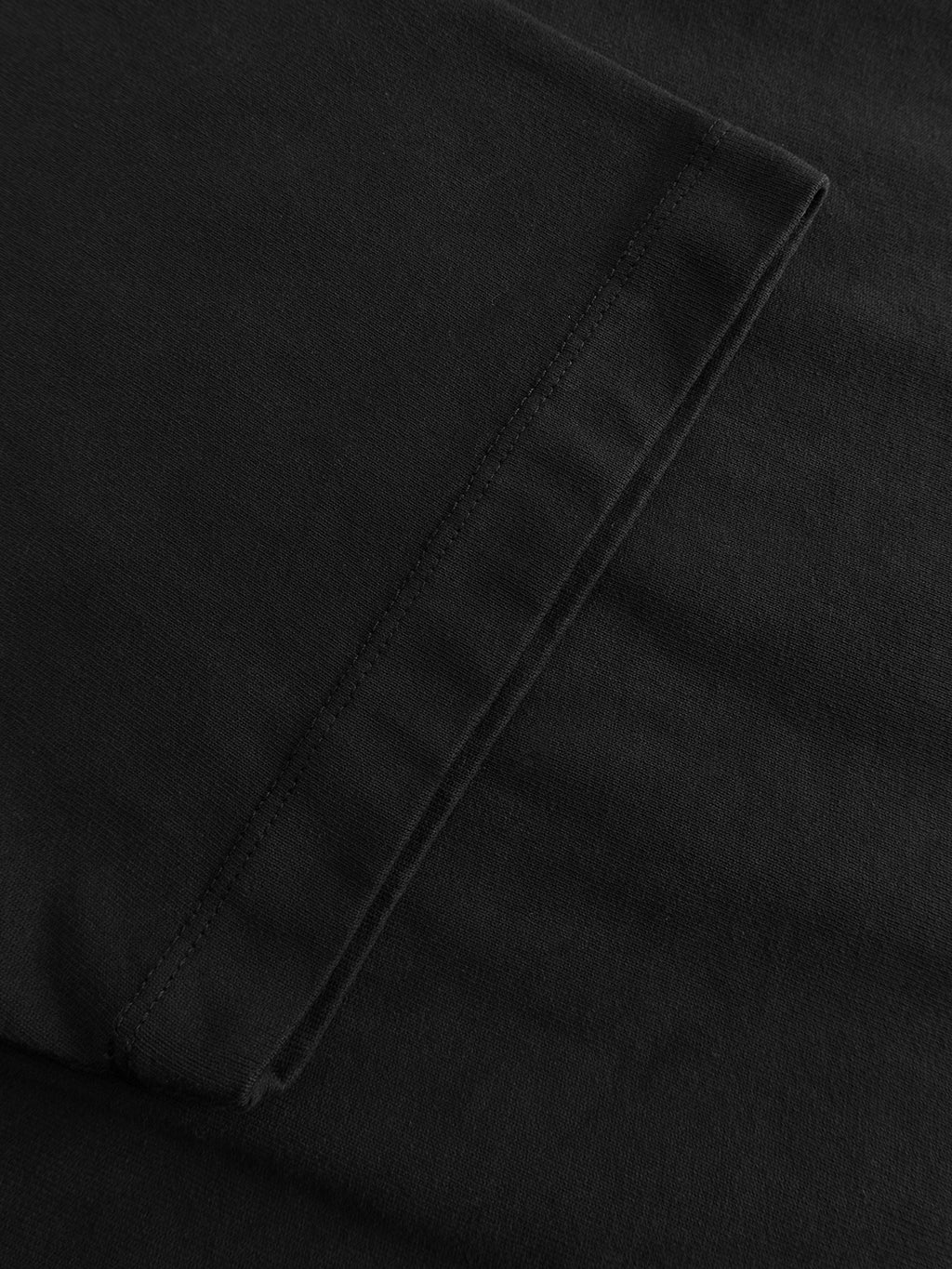 A close-up of the GABlegin Wix Boxy Hour SS T-shirt in black by Gabba, showcasing its mid-weight cotton jersey fabric with visible stitching and a folded edge, likely from a sleeve or hem. The garment suggests a relaxed boxy fit and features an embroidered Gabba logo for a subtle finishing touch.