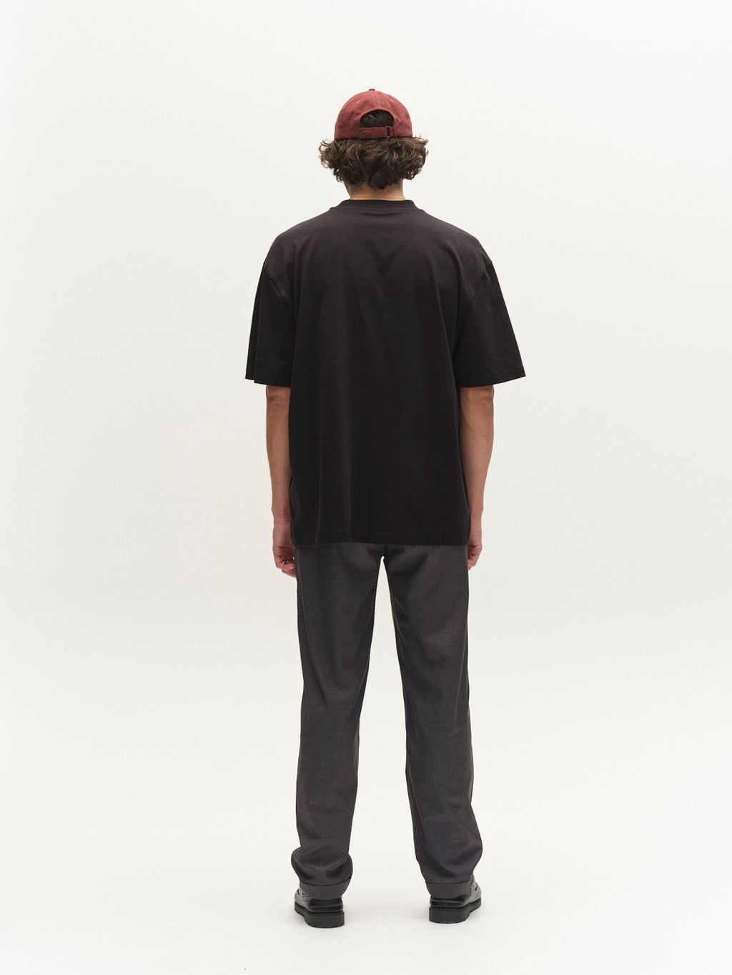 A person stands facing away from the camera wearing a black T-shirt, Gabba GABjoe Turnup Fin Pant in Lt. Grey, black shoes, and a red cap, against a plain white background.