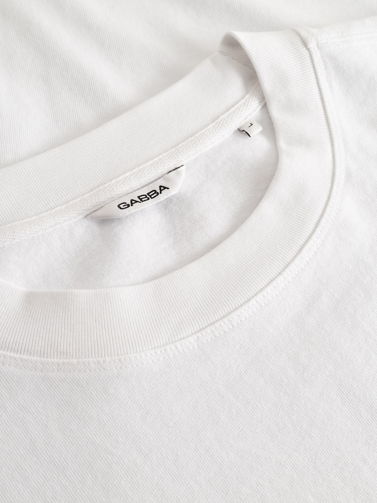 Close-up of the GABlegin Boxy Fiore SS T-Shirt in white by Gabba, crafted from textured cotton jersey with a visible Gabba label inside the collar. The image highlights the fabric’s unique texture, relaxed boxy fit, and meticulous stitching details—making it an ideal contemporary wardrobe staple.