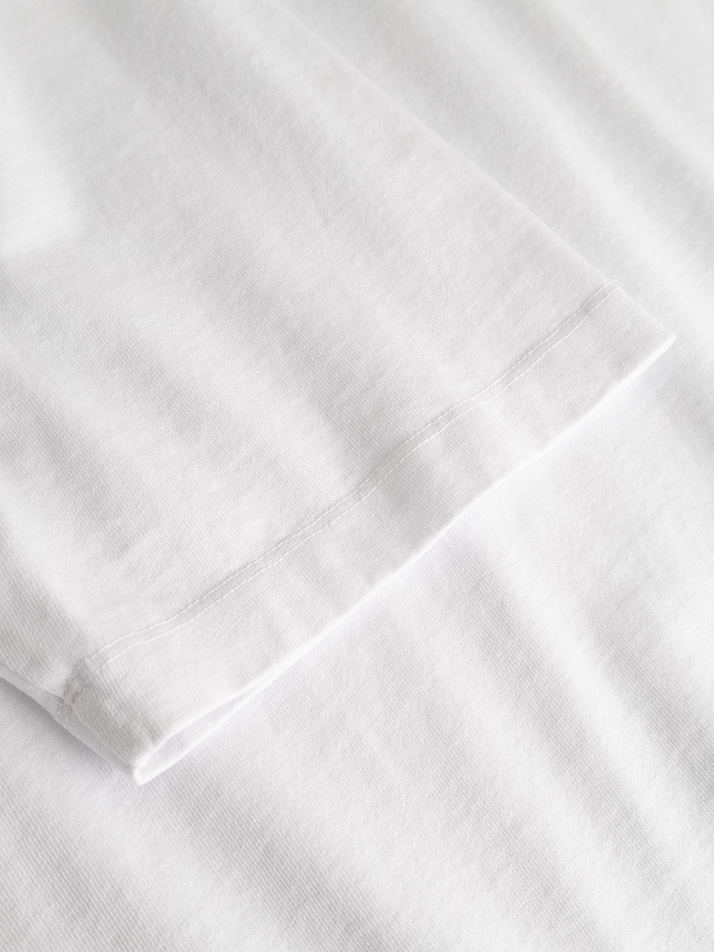 Close-up of the sleeve and fabric of the Gabba GABlegin Boxy Fiore SS T-Shirt in white, crafted from textured cotton jersey, showcasing the fabric’s texture, precise stitching, and clean, minimal design set against a matching white background—an essential contemporary wardrobe staple.