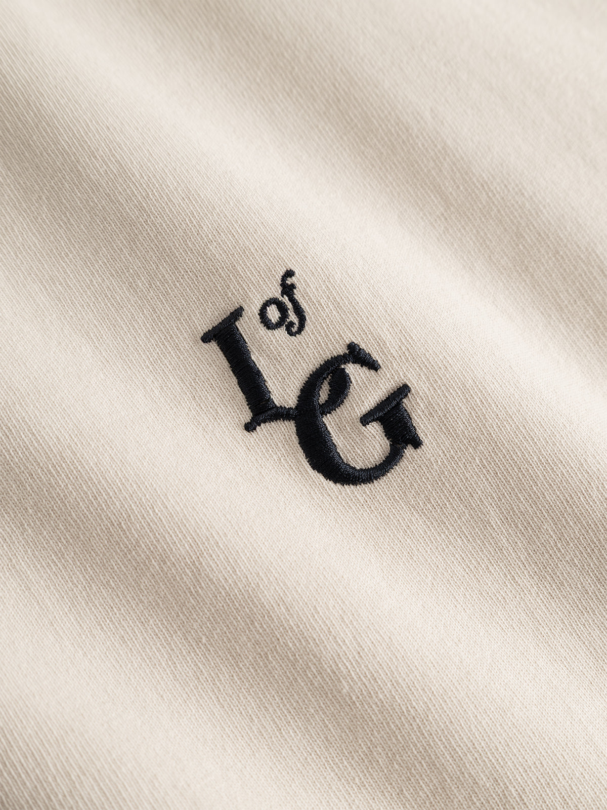 Close-up of the Gabba GABlegin Boxy Glory SS T-Shirt in Birch, showcasing its soft, slightly textured beige cotton jersey fabric with black “L of G” embroidered text.
