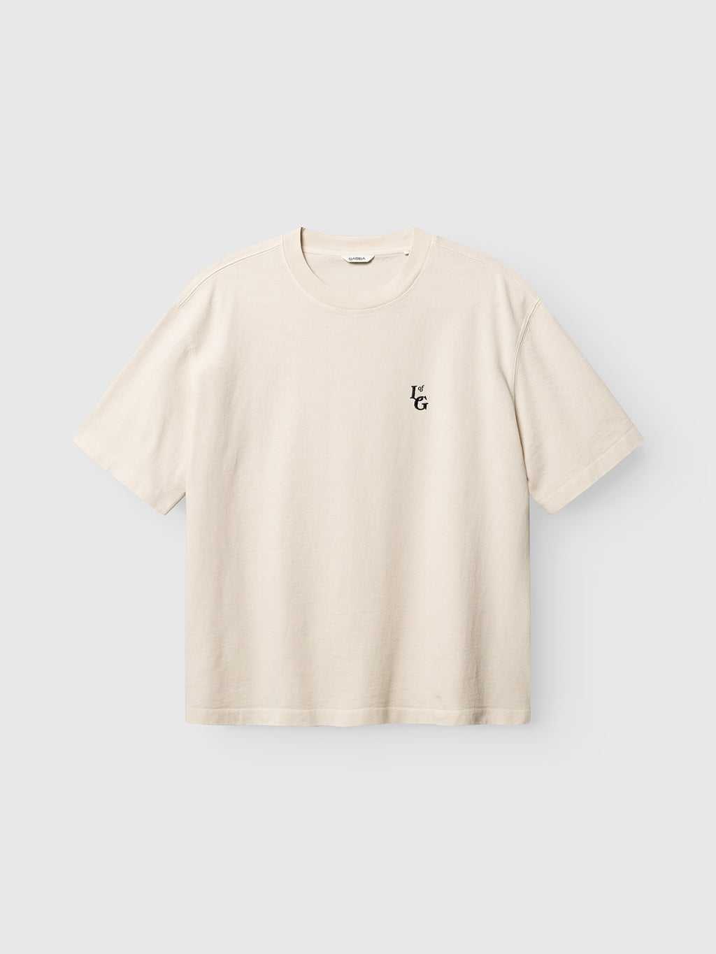 Gabba GABlegin Boxy Glory SS T-Shirt in Birch, a cream-colored, short-sleeve tee featuring a small black ‘TG’ logo on the left chest, made from textured cotton jersey in a relaxed boxy fit, shown against a plain light gray background.