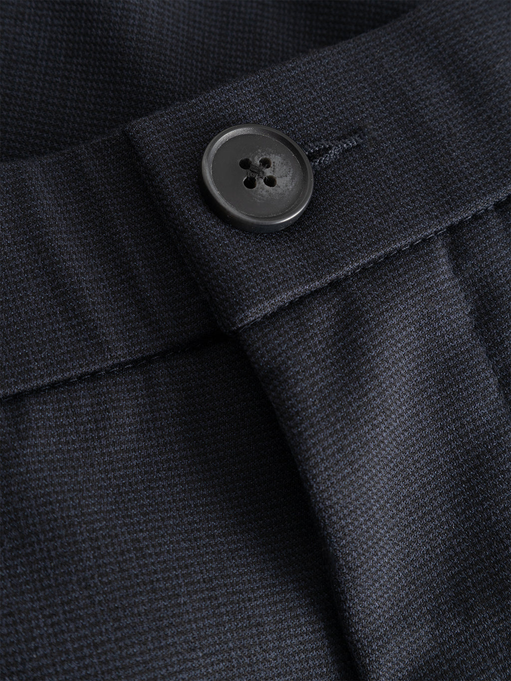 Close-up of a black button on the waistband of Gabba’s GABmonza Tasca Deme Pant in Dark Navy, highlighting the stitching details and the top part of the zipper fly on the micro-patterned fabric.
