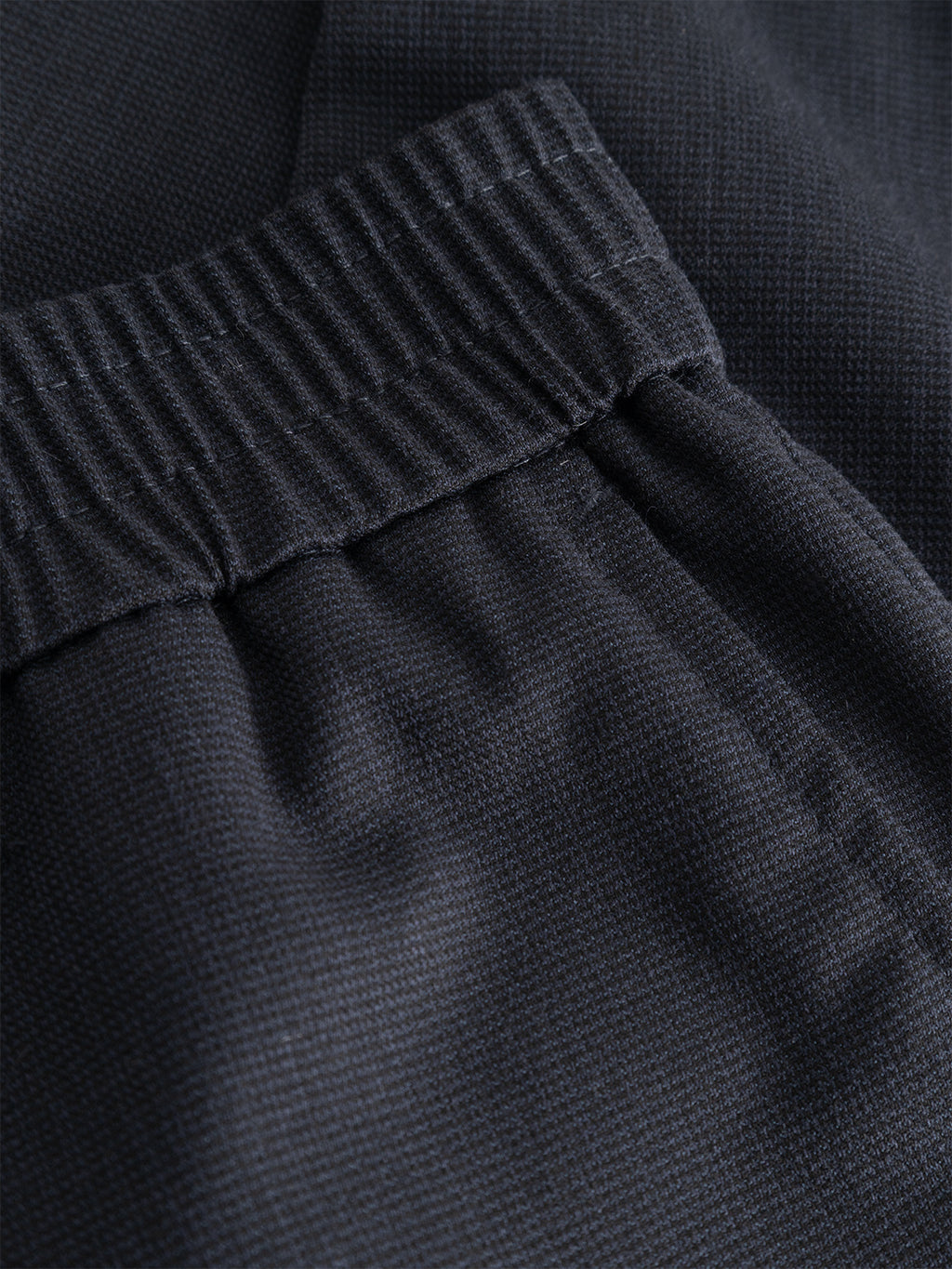 Close-up of the GABmonza Tasca Deme Pant by Gabba in dark navy, featuring a micro-patterned fabric and elastic waistband. The detailed texture and stitching emphasize the brand’s quality craftsmanship and showcase the pant’s relaxed straight fit.
