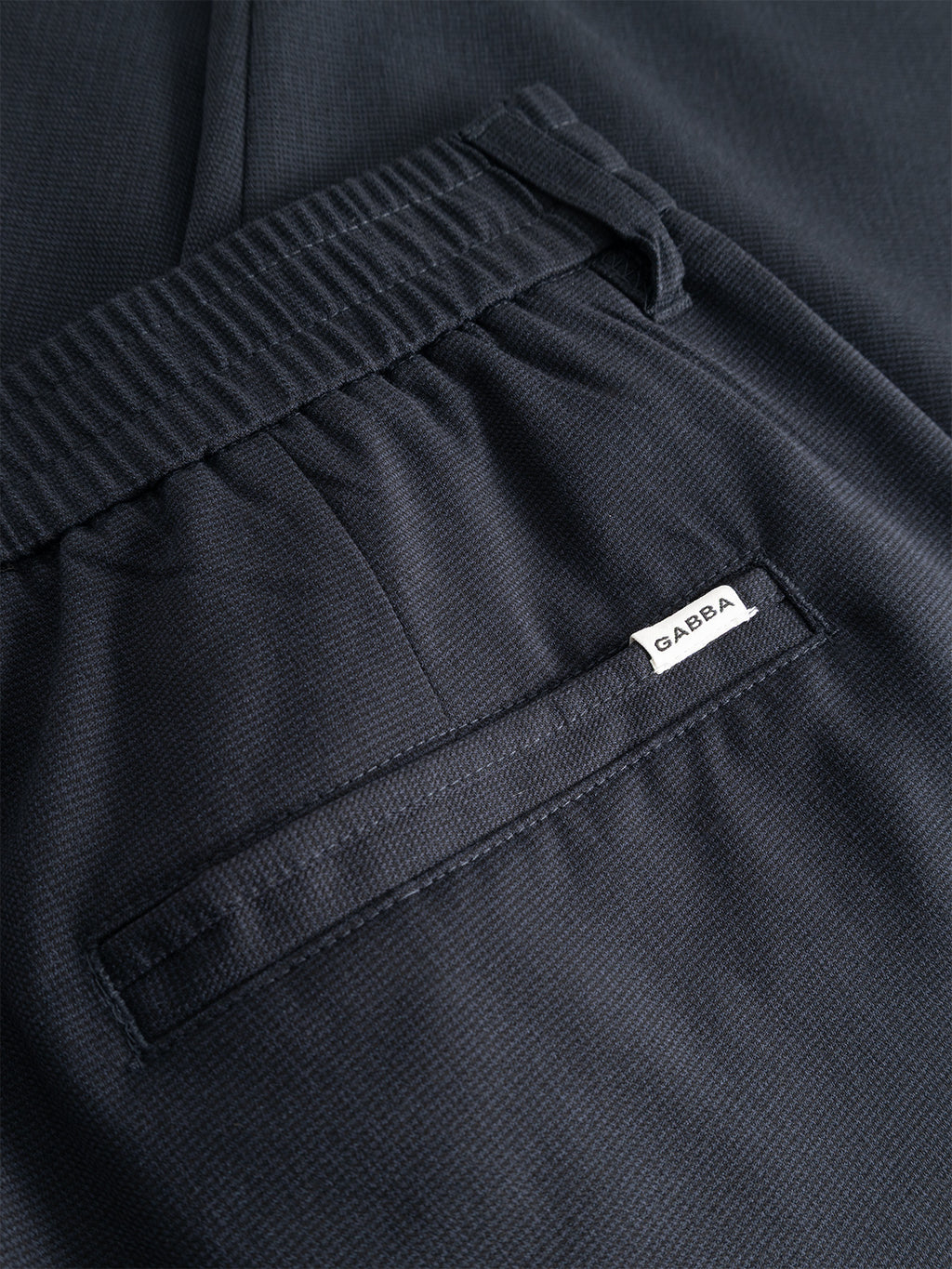 Close-up of the back pocket and waistband of the Gabba GABmonza Tasca Deme Pant in dark navy, featuring micro-patterned fabric with an elastic band. A small white tag with “Gabba” is sewn near the pocket seam.
