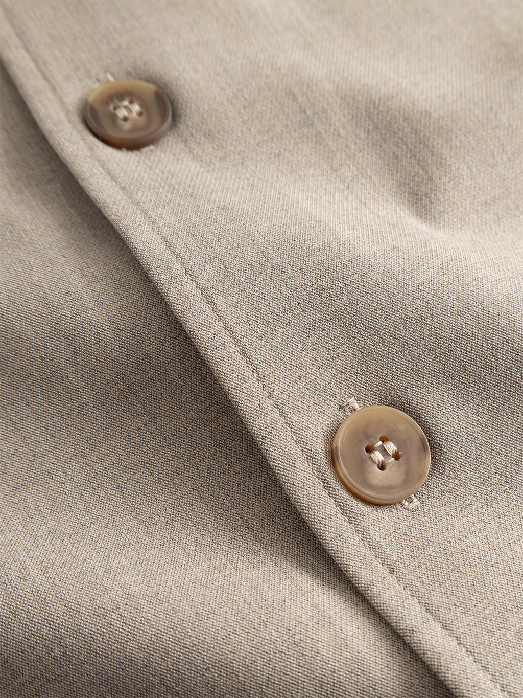 Close-up view of two brown buttons sewn onto light beige fabric, likely part of the Gabba GABtogger Push Phin LS Overshirt GRS - Sand. The fabric, crafted from a soft wool-viscose blend, features a smooth texture and a subtle weave pattern.