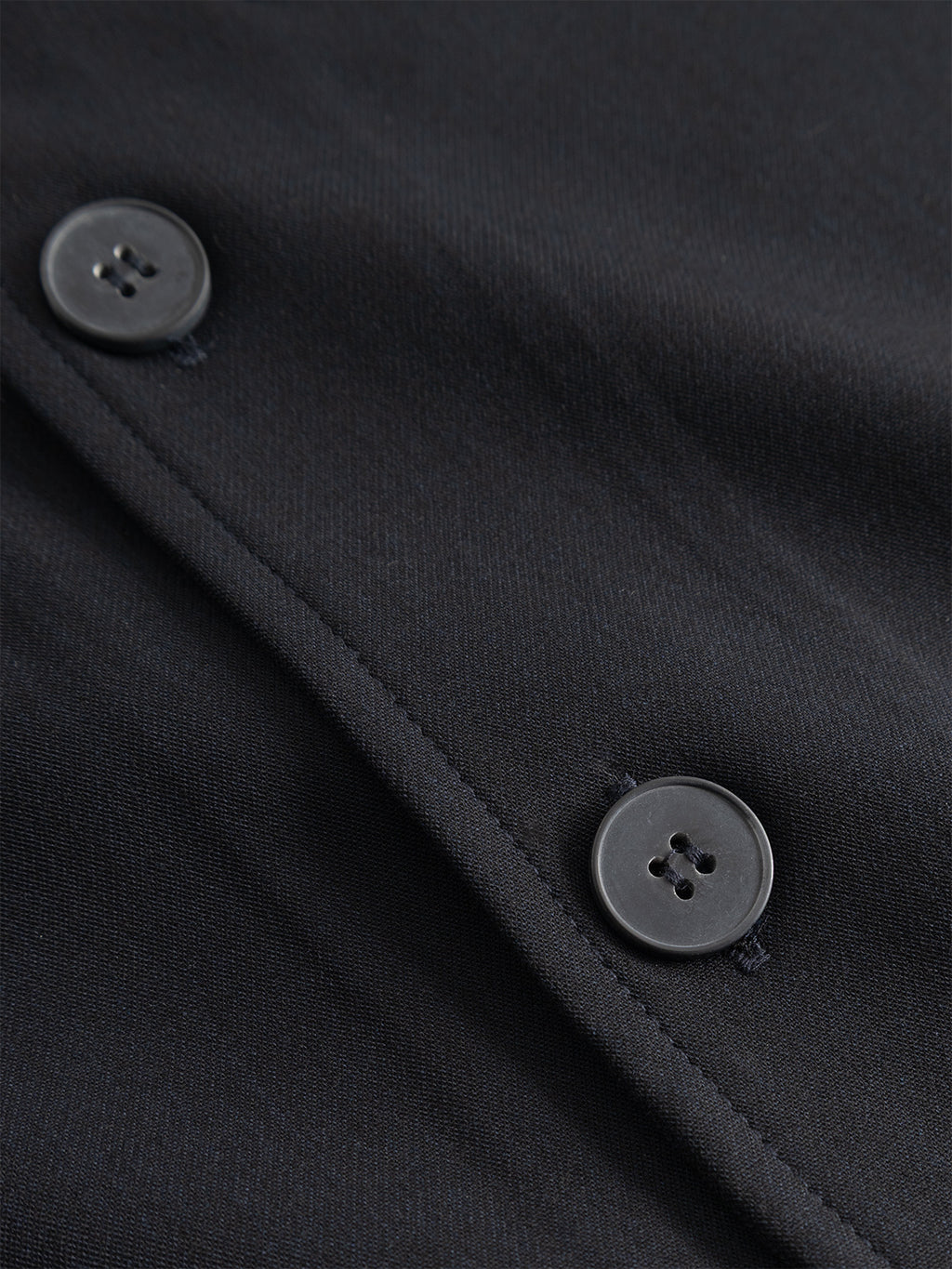 Close-up of the Gabba GABtogger Push Phin LS Overshirt GRS in Blue Black, crafted from a wool-viscose blend fabric with two matching black buttons sewn beside a seam, highlighting texture and stitching details—an ideal layering essential.