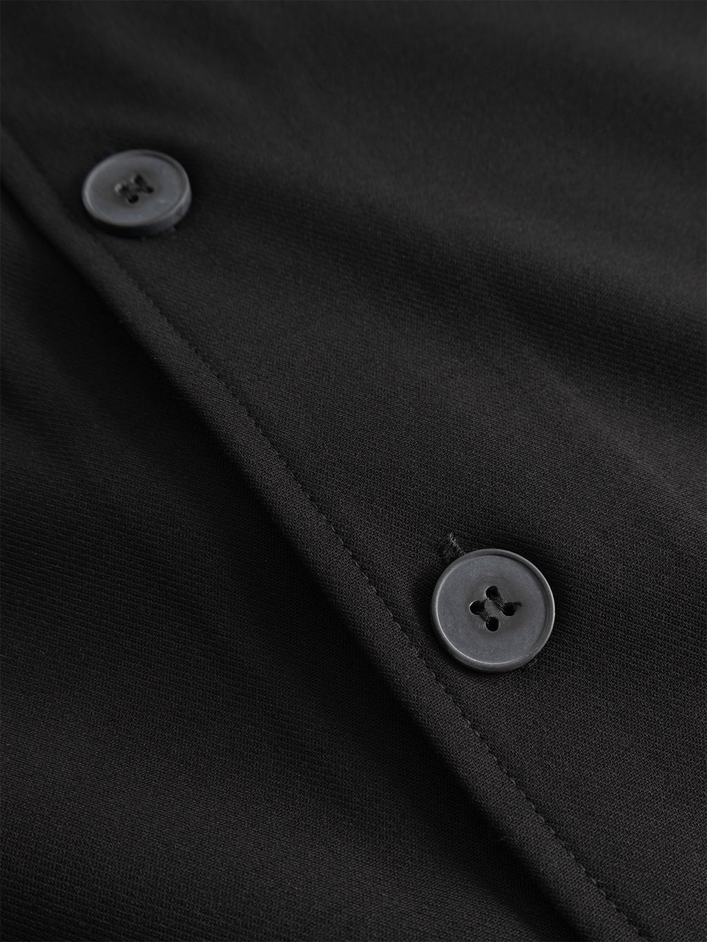 Close-up of two black buttons sewn onto the black wool-viscose blend fabric of the Gabba GABtogger Push Phin LS Overshirt GRS, positioned parallel to the seam—an essential layering piece.
