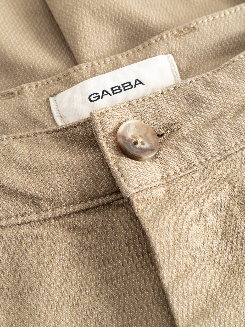 Close-up of the Gabba GABjoe-pas Dale Pant in Sand, featuring a tan button and a white waistband label reading “GABBA.” The high-stretch cotton-blend fabric and precise stitching details are clearly visible.