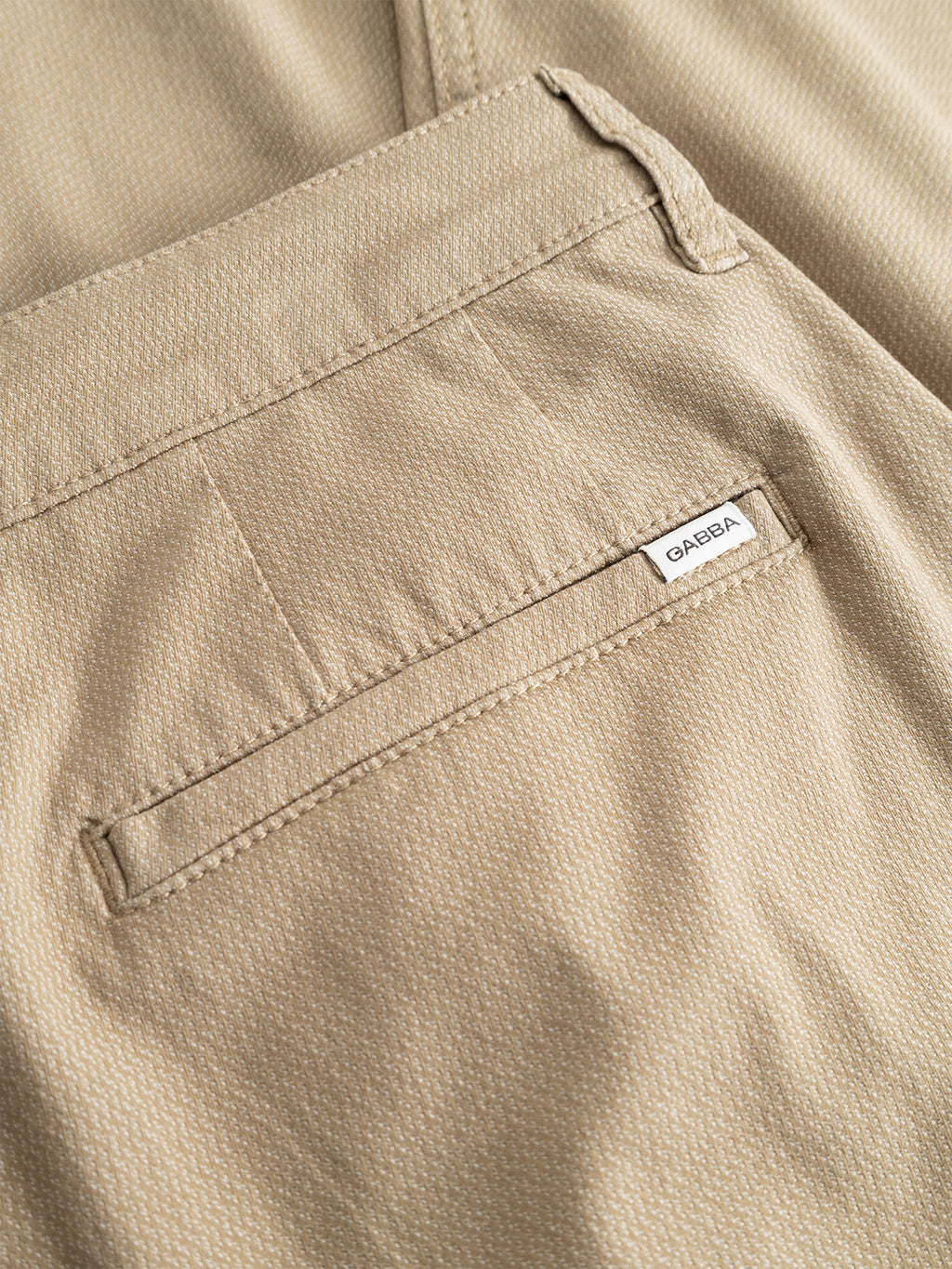 Close-up of the back pocket on the Gabba GABjoe-pas Dale Pant in Sand, featuring a small white Gabba label. The tapered fit pants are made from a high-stretch cotton-blend material with a subtle textured pattern and precise stitching details.