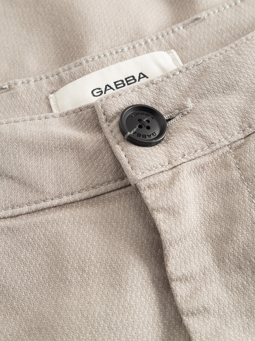 Close-up of the Gabba GABjoe-pas Dale Pant in Grey Paloma, highlighting the black button with Gabba text, a belt loop, and a white label stitched with the Gabba brand inside the waistband. The high-stretch cotton-blend fabric texture is clearly visible.