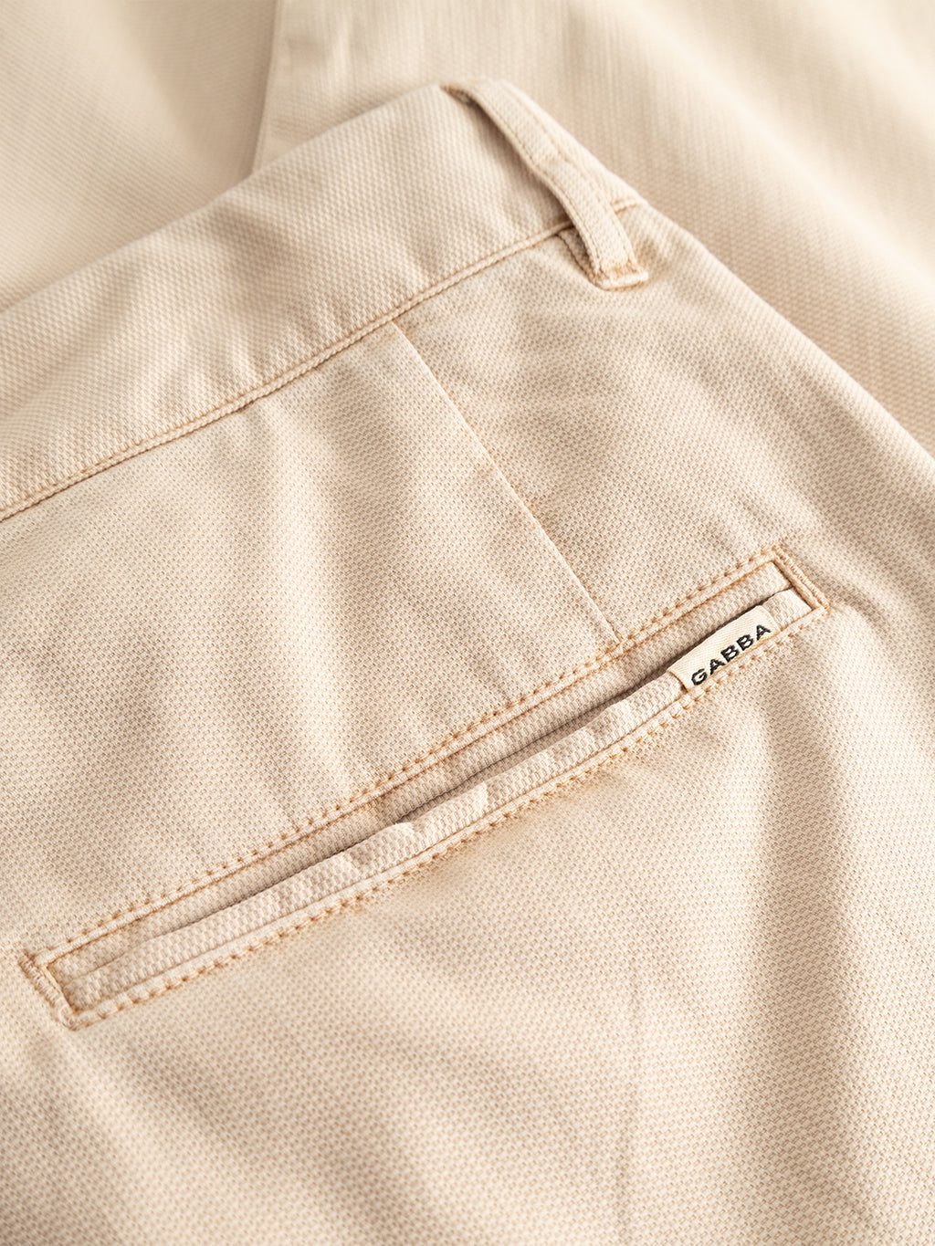 Close-up of the pocket on the GABfirenze Cropped Marlo Pant in Birch by Gabba, showcasing a small white Gabba tag sewn near the edge of the welt pocket. The garment is crafted from garment-dyed dobby fabric with a subtle textured pattern.