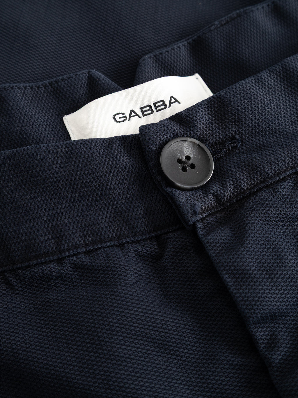 Close-up of the GABfirenze Cropped Marlo Pant in Dark Navy, crafted from garment-dyed dobby fabric, featuring a black button and a white Gabba brand label.