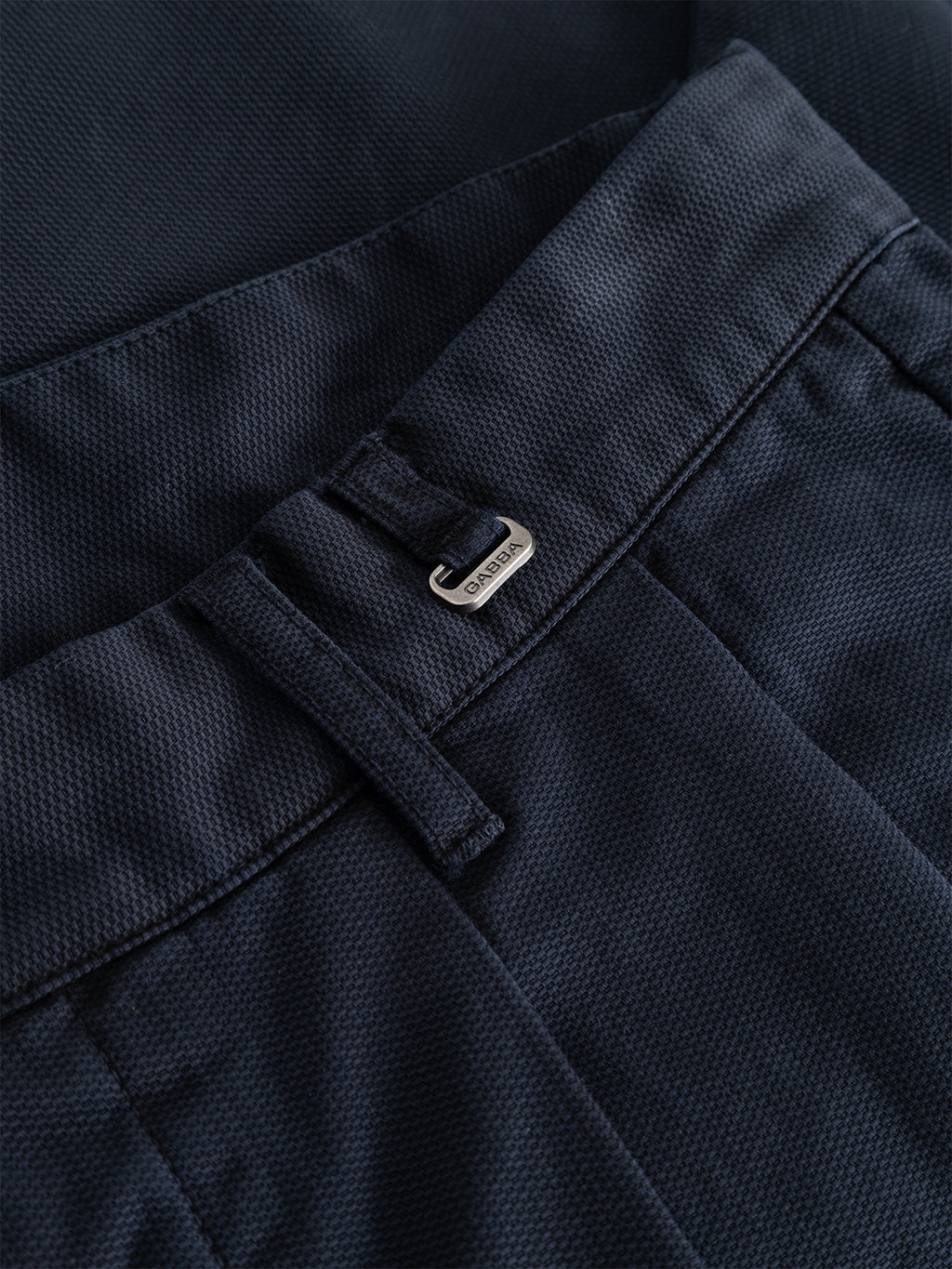 Close-up of the Gabba GABfirenze Cropped Marlo Pant in dark navy, showcasing its relaxed fit and silver waistband clasp engraved with a subtle logo. The garment-dyed dobby fabric presents a sturdy construction and refined pattern, combining comfort with elevated style.