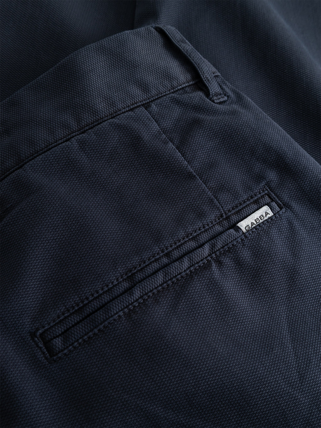 Close-up of the back pocket of the GABfirenze Cropped Marlo Pant in Dark Navy by Gabba, featuring a small white tag reading GABBA stitched near the pocket opening and crafted from garment-dyed dobby fabric.