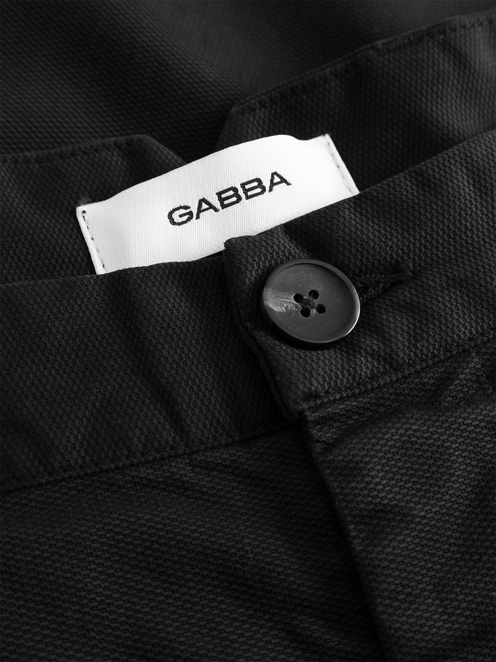 Close-up of the Gabba GABfirenze Cropped Marlo Pant in black, crafted from garment-dyed dobby fabric with a textured finish, featuring a black button and a partially visible white Gabba label above the waistband.
