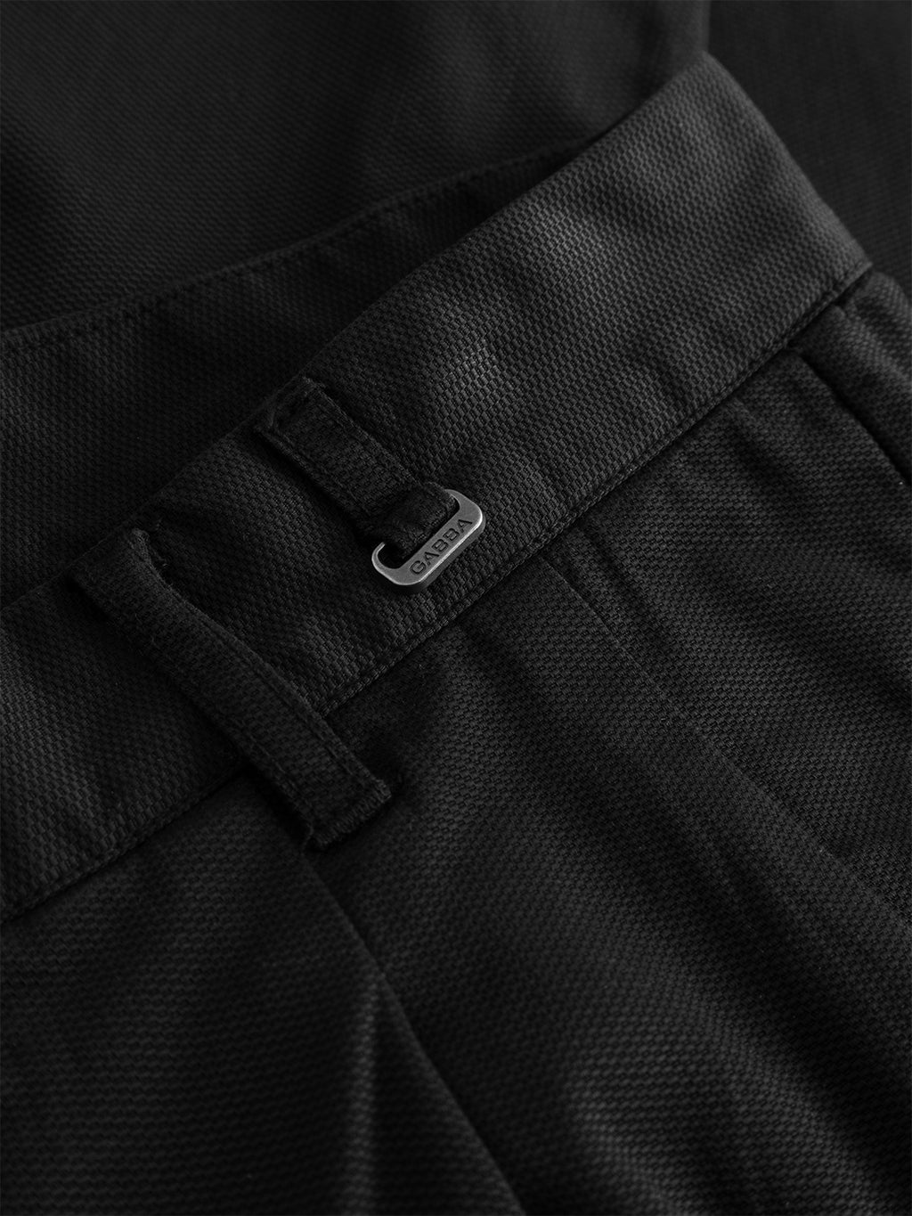 Close-up of the black GABfirenze Cropped Marlo Pant by Gabba, featuring a textured dobby fabric with garment-dyed finish, visible waistband, belt loop, front pocket, and a small metallic Gabba logo tag attached near the belt loop.