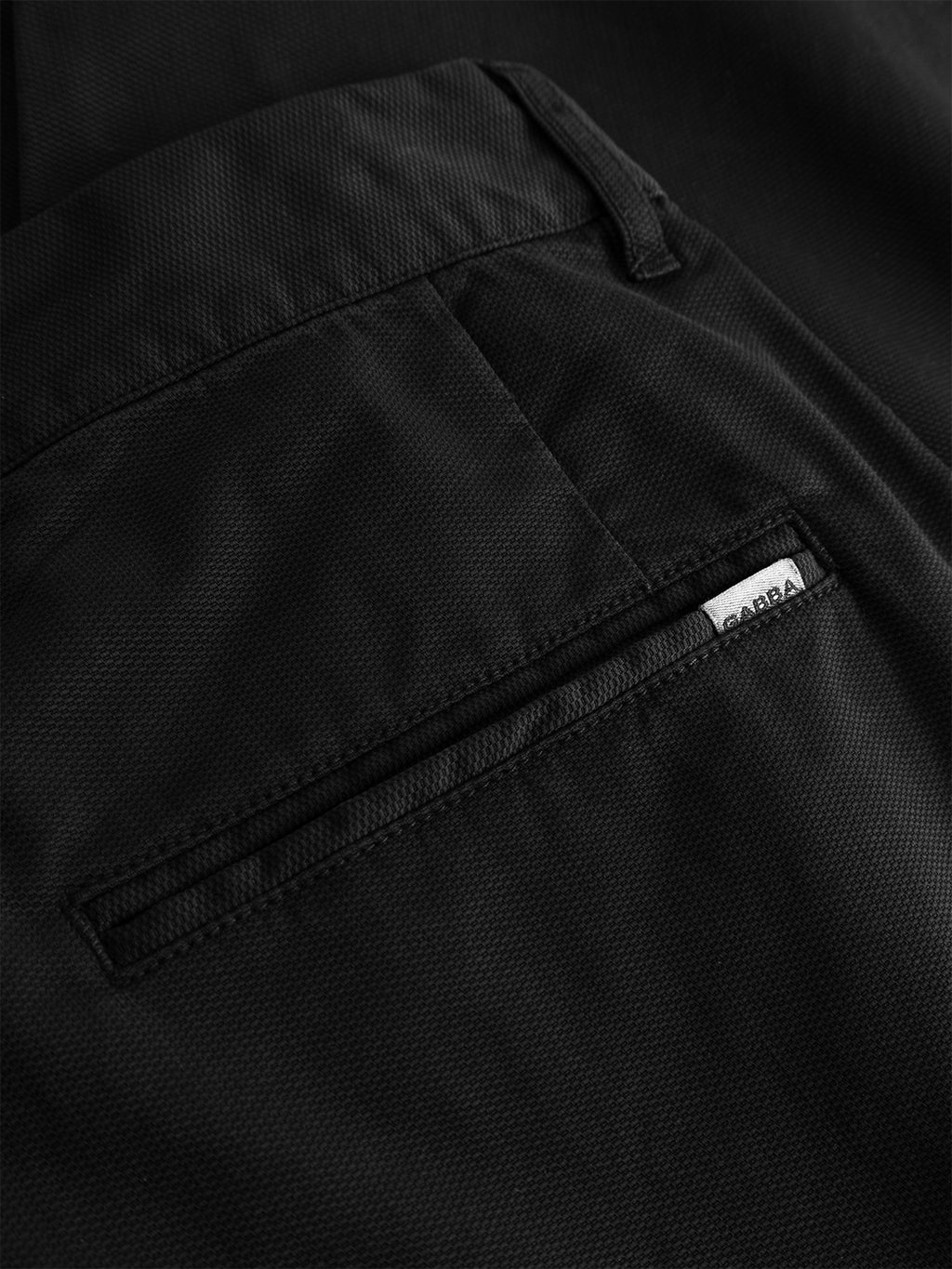 Close-up of the GABfirenze Cropped Marlo Pant in black by Gabba, showcasing a pocket with a visible seam and a small white label bearing the word GARPA near the pocket opening. The garment-dyed dobby fabric features a subtle textured pattern.
