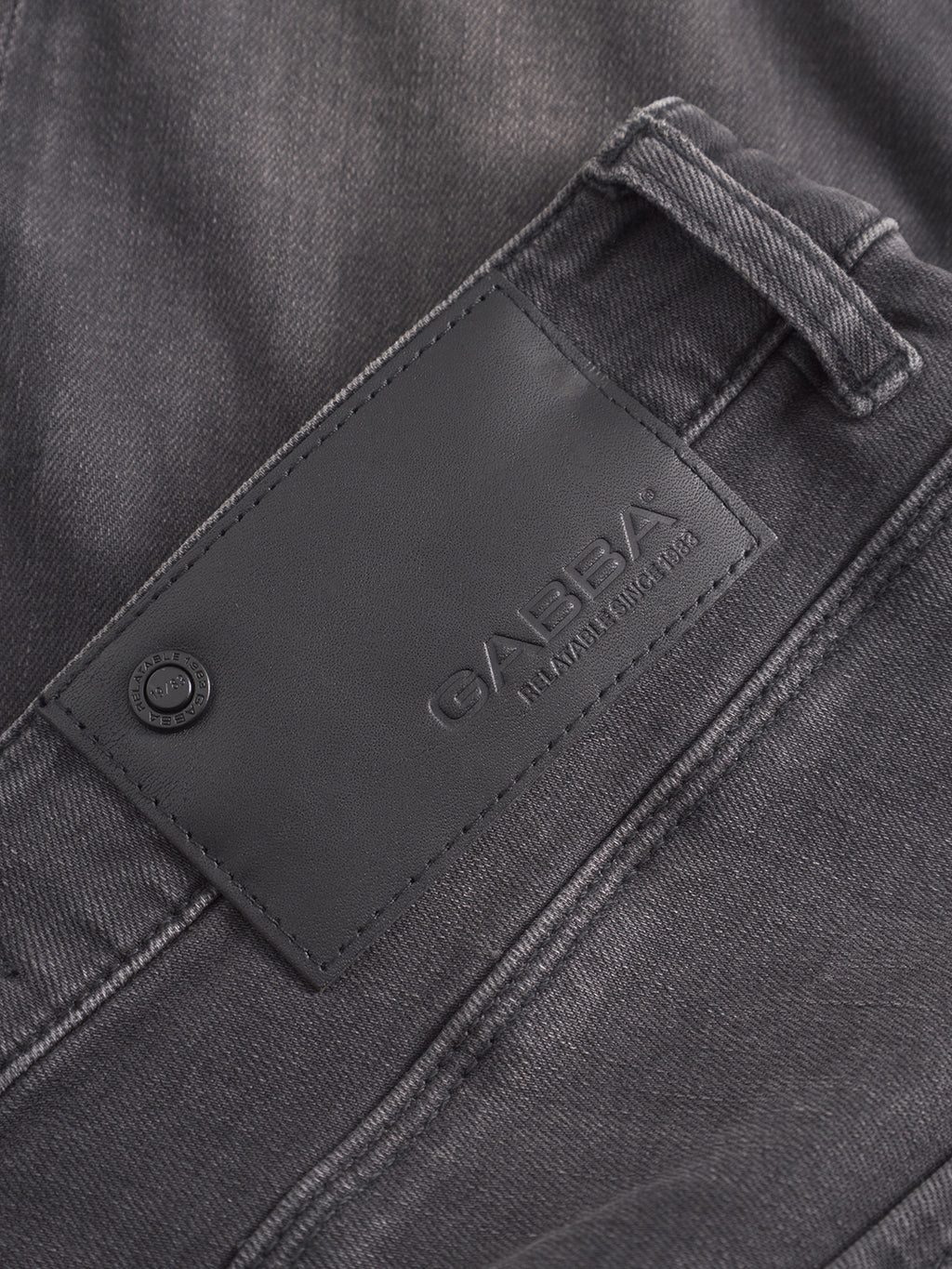 Close-up of gray GABrey Thor Jeans by GABBA, showcasing a black leather brand patch with 