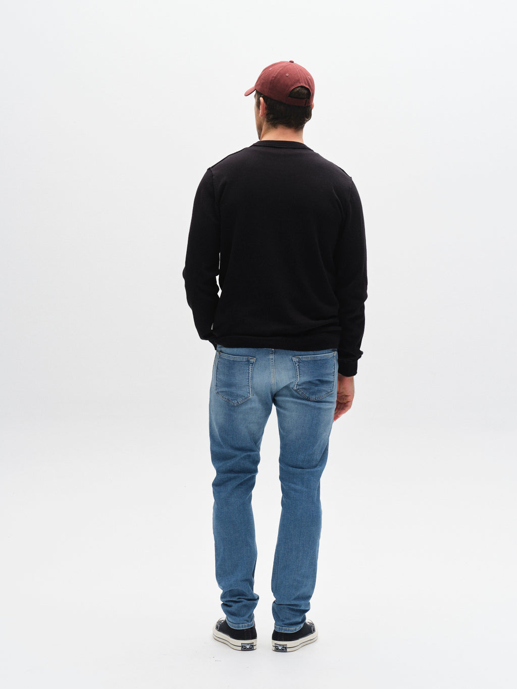A man faces away from the camera, wearing a burgundy cap, black long-sleeve shirt, sneakers, and GABBA GABjones K2615 Lt. - Denim wash slim fit jeans with high flexibility, against a plain white background.