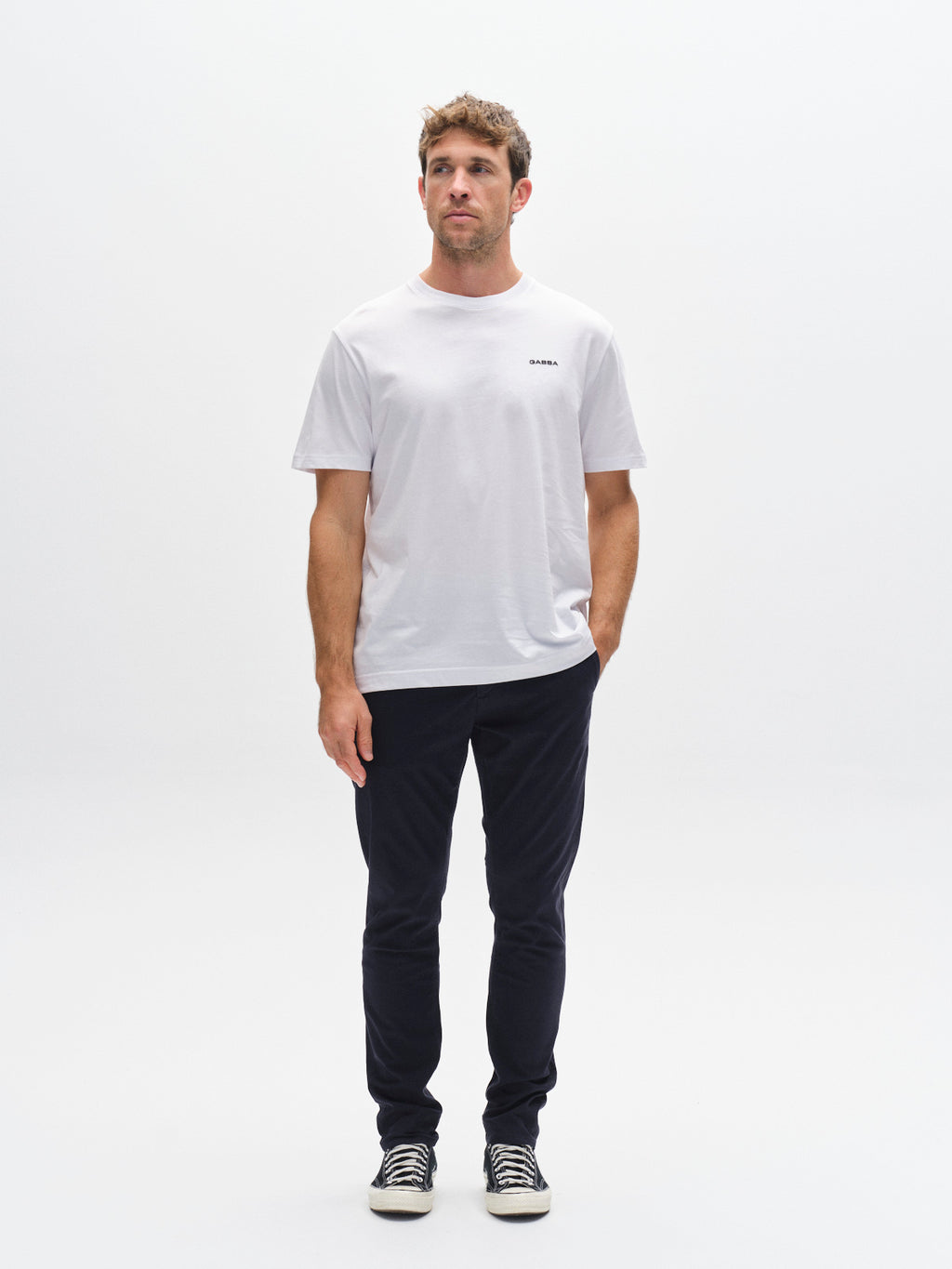 A man stands against a white background, wearing a white t-shirt and the GABBA GABpaul K3280 Dale Chino in Navy with French and double-paspel back pockets. He looks to the side with a neutral expression; black sneakers complete his look.