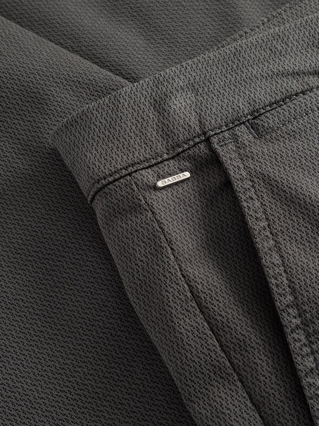 Close-up of dusty sage green Paul K3280 Dale chino pant by Gabba, featuring textured fabric, slim fit, French pockets, and a small silver DAMA tag sewn near the waistband above a seam.