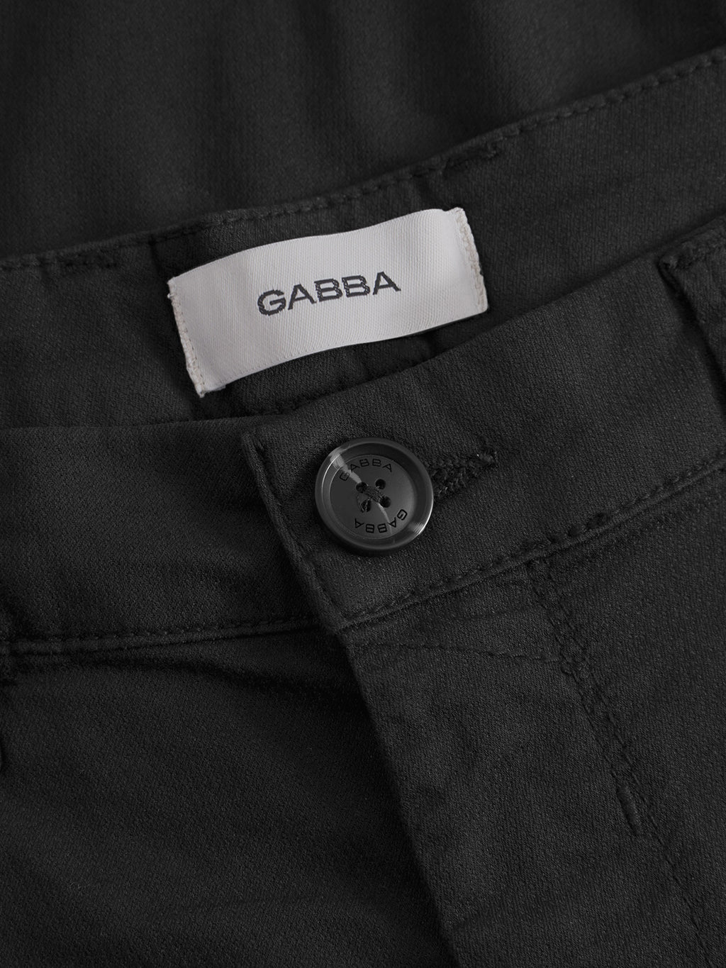 Close-up of the waistband on GABBA’s GABpaul K3280 Dale Chino - Black, featuring a black button, visible stitching, and a white GABBA label. Includes French pockets and double paspel back pockets for added style.