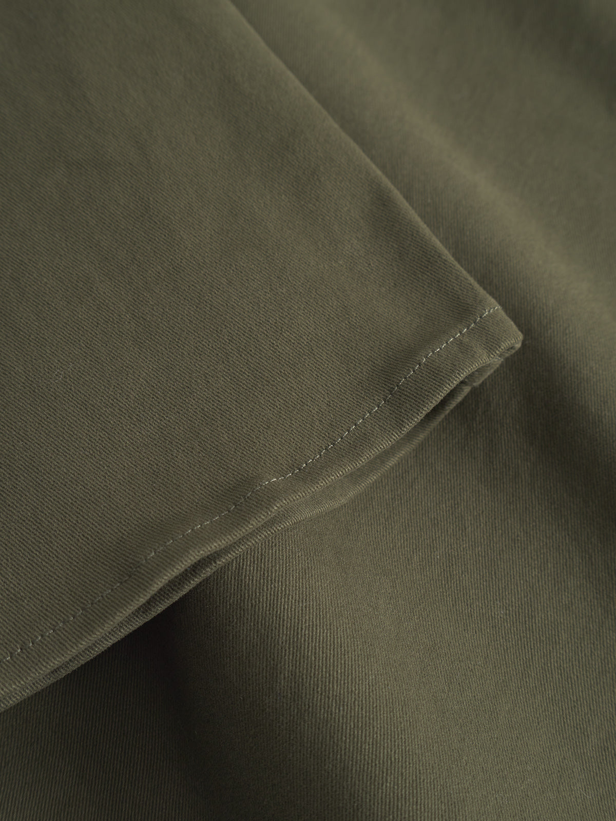 Close-up of the GABtopper LS Shirt - Army by GABBA reveals olive green fabric with visible hem stitching, showcasing its textured weave. The soft material is slightly folded, making it ideal for layering as an overshirt.