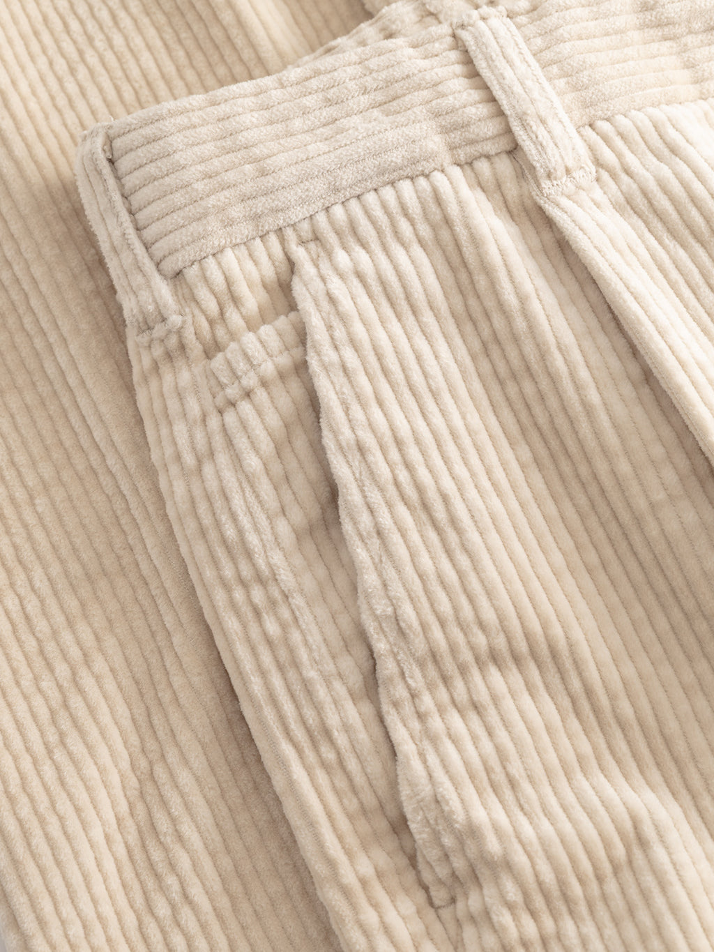 Close-up of the Gabba GABnapoli 19 Ibre Pant in Birch, highlighting the textured beige cotton corduroy fabric with prominent vertical ridges, detailed waistband, and pockets. These men’s tailored pants are laid flat on a matching corduroy background.