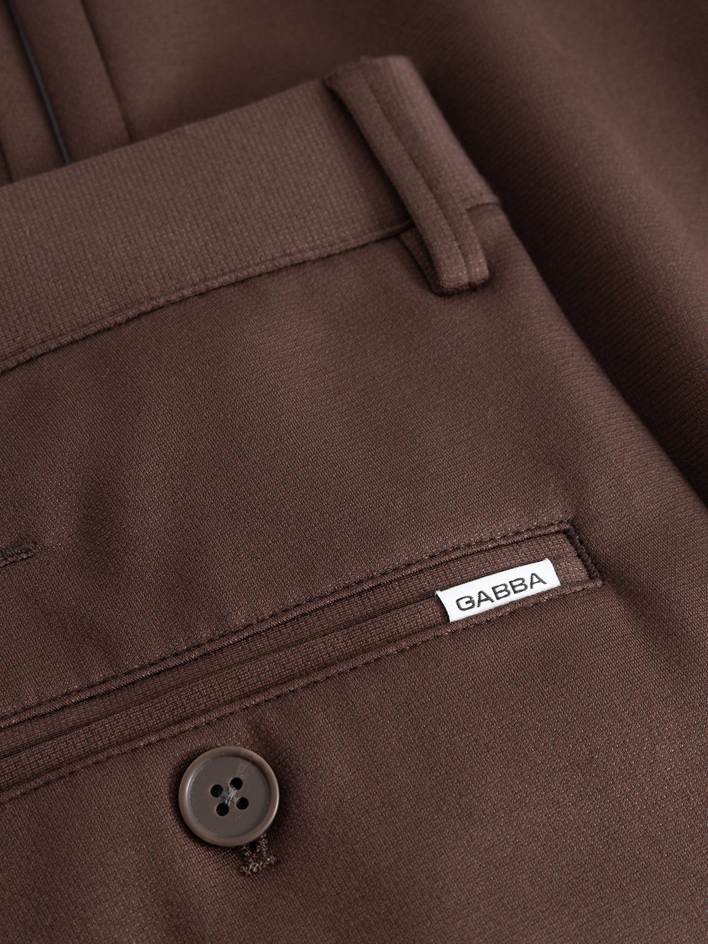 Close-up of the GABpaul Dotty Pant in Brown Slate by Gabba, highlighting the slim chino fit’s pocket with a button and a small white Gabba tag sewn above it. The smooth, slightly textured fabric features a subtle micro-pattern weave that adds sophistication to the overall design.