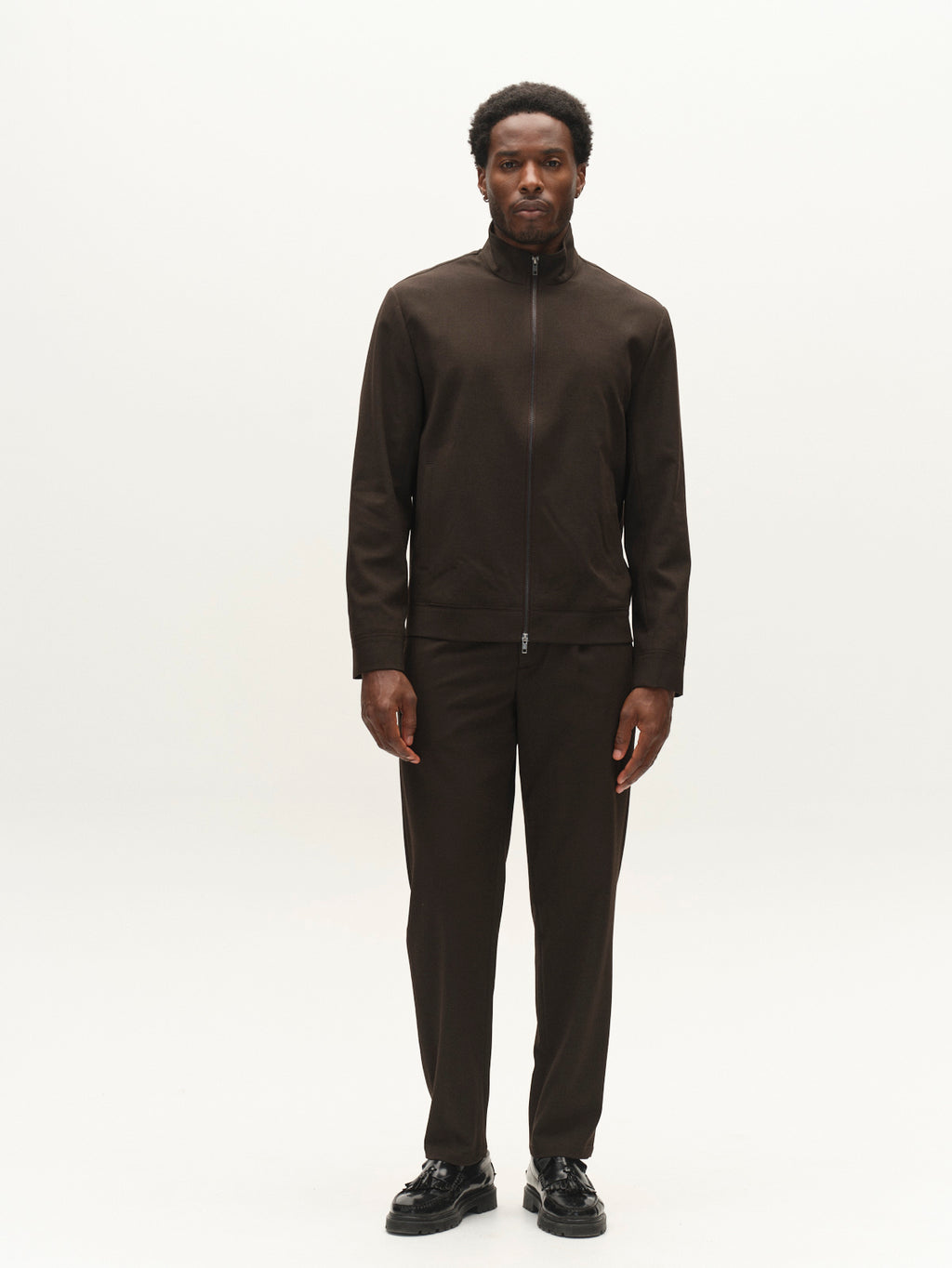 A man stands facing forward against a plain white background, wearing the Gabba GABnik Phin GRS - Brown Slate men’s regular fit jacket made from a wool and viscose blend—an ideal choice for modern outerwear—with matching pants and black shoes.