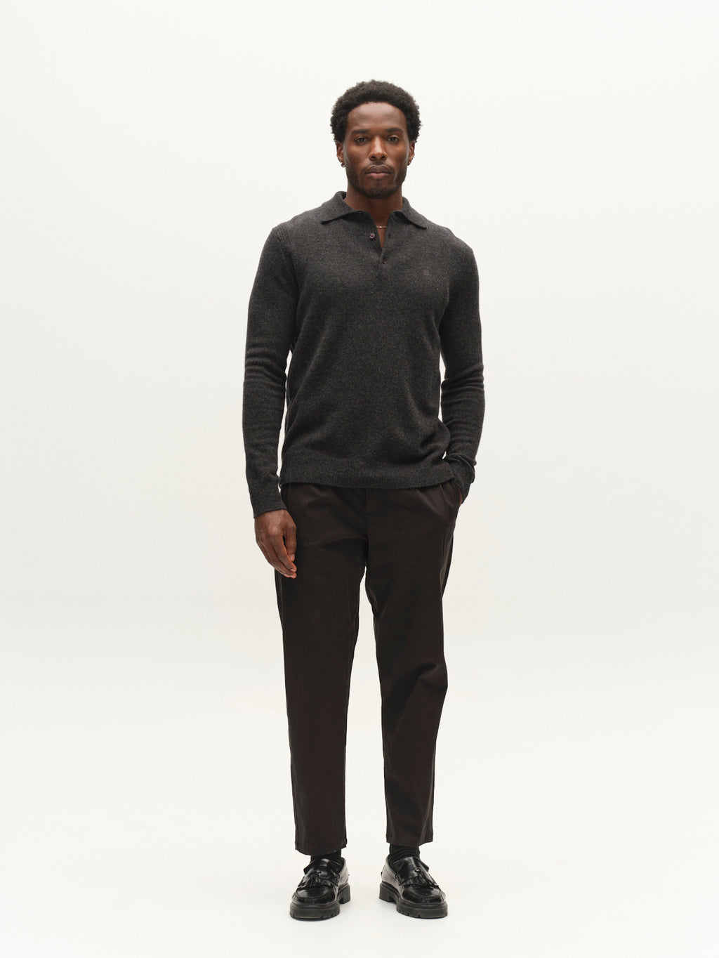 A man stands against a plain white background, wearing a dark long-sleeve polo shirt, black Gabba GABfirenze Bolu Cropped TENCEL™ Pants, and black shoes, with one hand in his pocket.