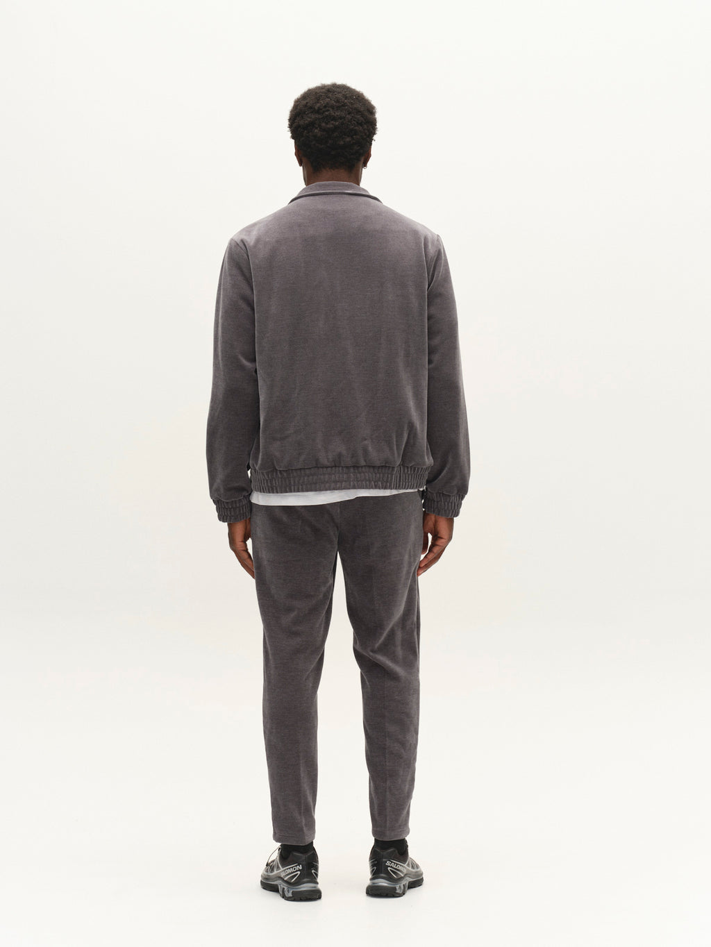 A person stands facing away, wearing the Gabba GABnik Pulz Fune Jacket in Turbulence Blue, paired with black sneakers, against a plain white background.