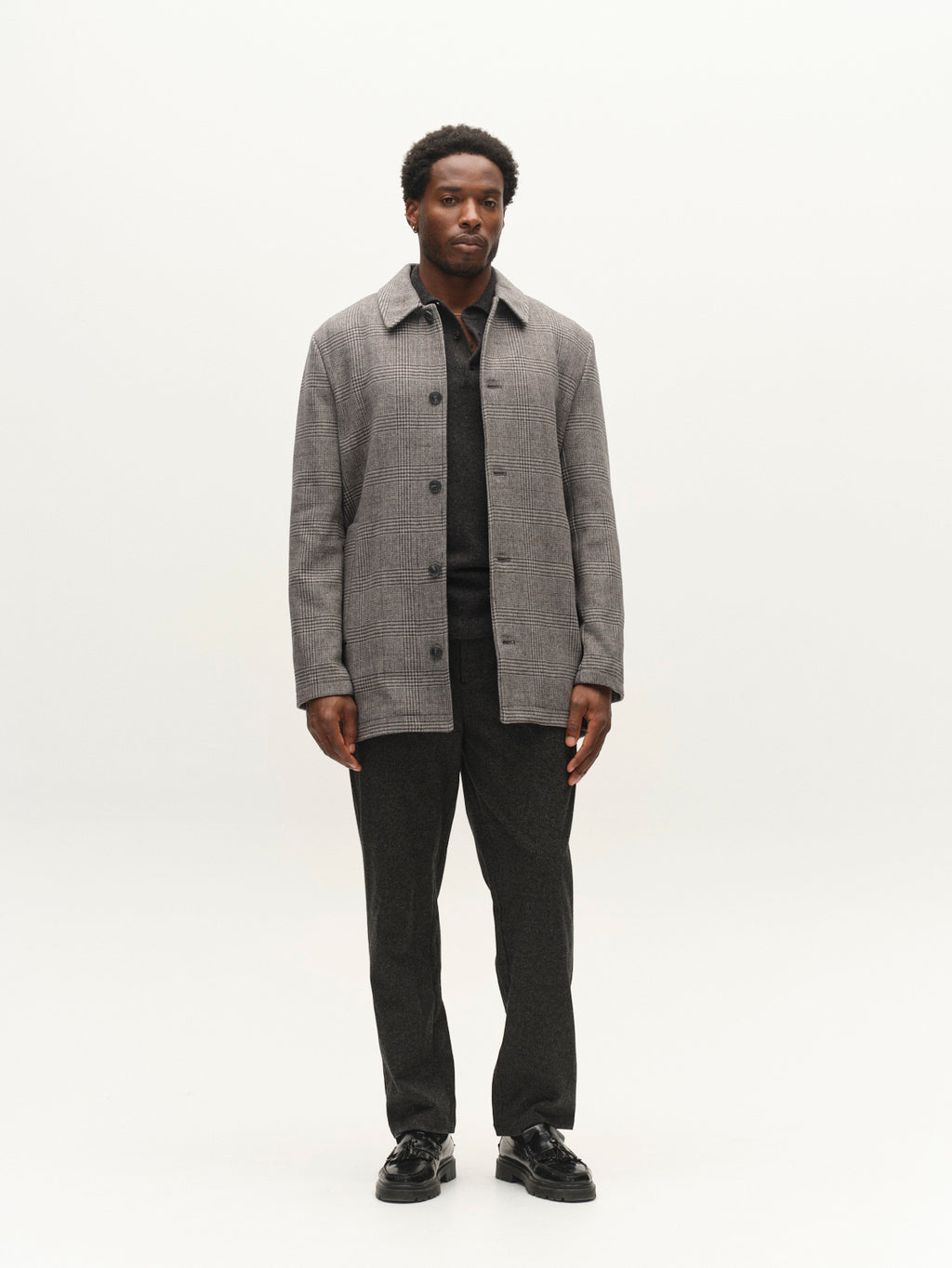 A man stands facing forward, wearing the Gabba GABowen Scacco Coat in grey check—a regular fit button-up coat crafted from wool-blend checked fabric—layered over a black shirt and dark pants, with black shoes, against a plain white background.