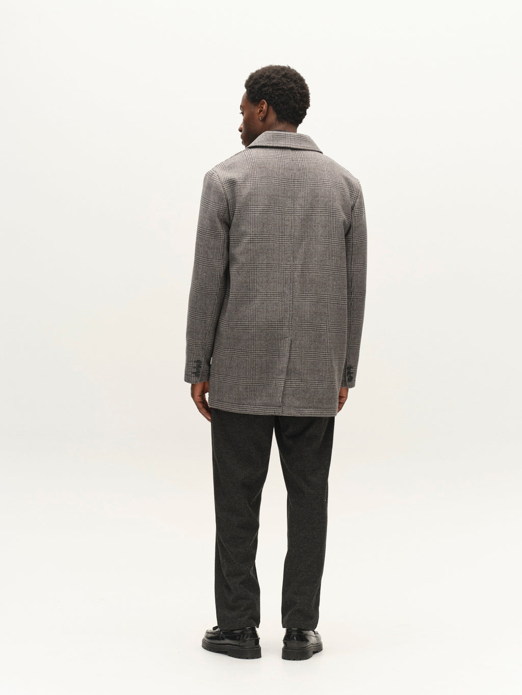 A person stands facing away, wearing the Gabba GABowen Scacco Coat in Grey Check—a regular fit coat crafted from wool-blend checked fabric—paired with dark pants and black shoes against a plain white background.